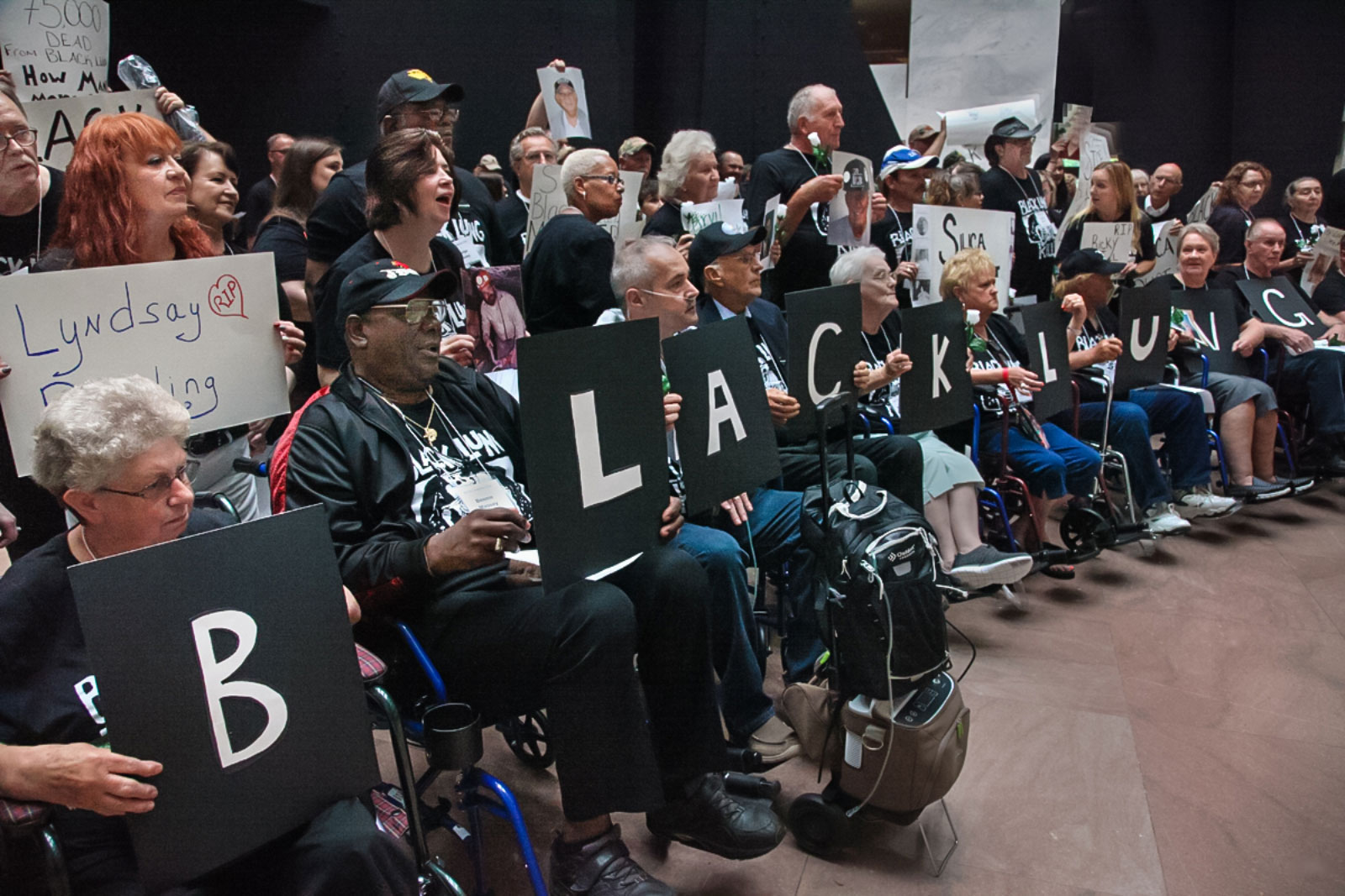 Large group of people, some in front holding signs with individual letters spelling out the words "black lung"