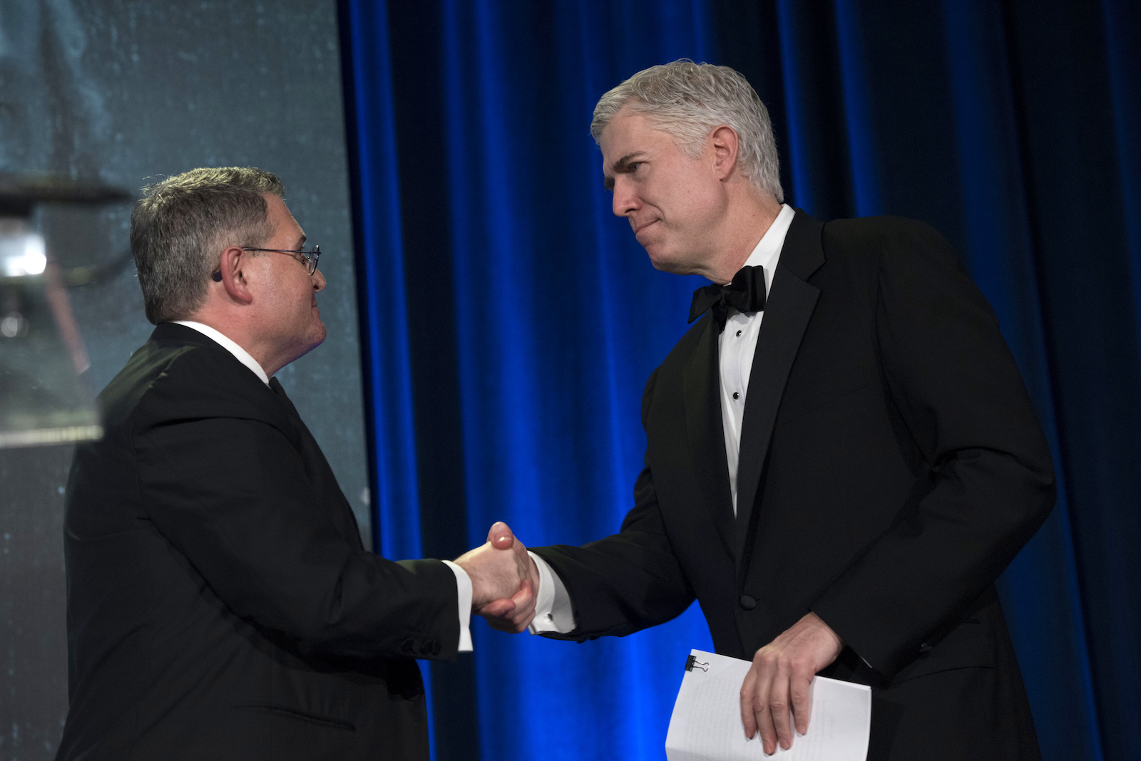 two men in tuxedos shake hands