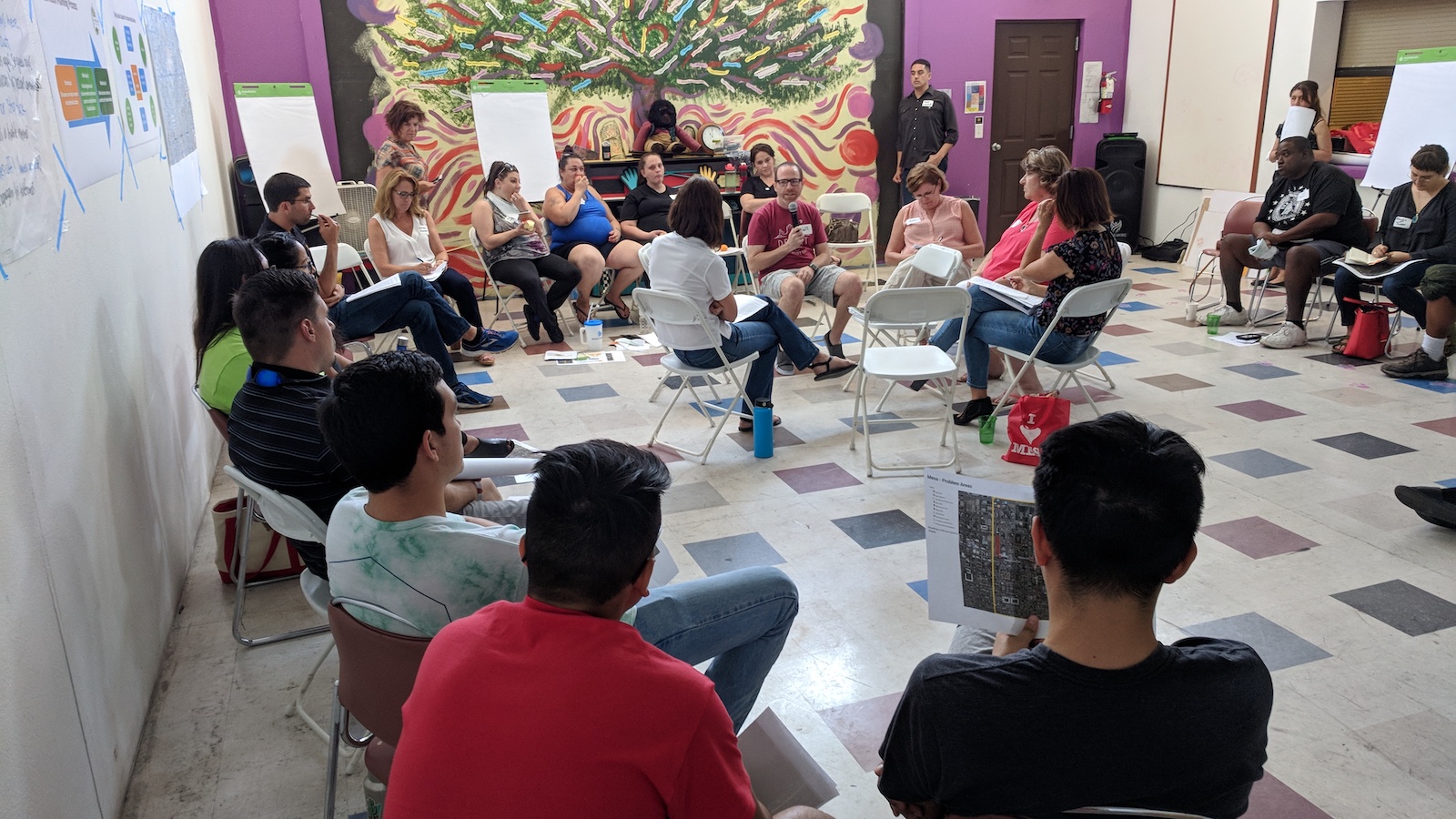 people sit on folding chairs in a circle inside of a classroom