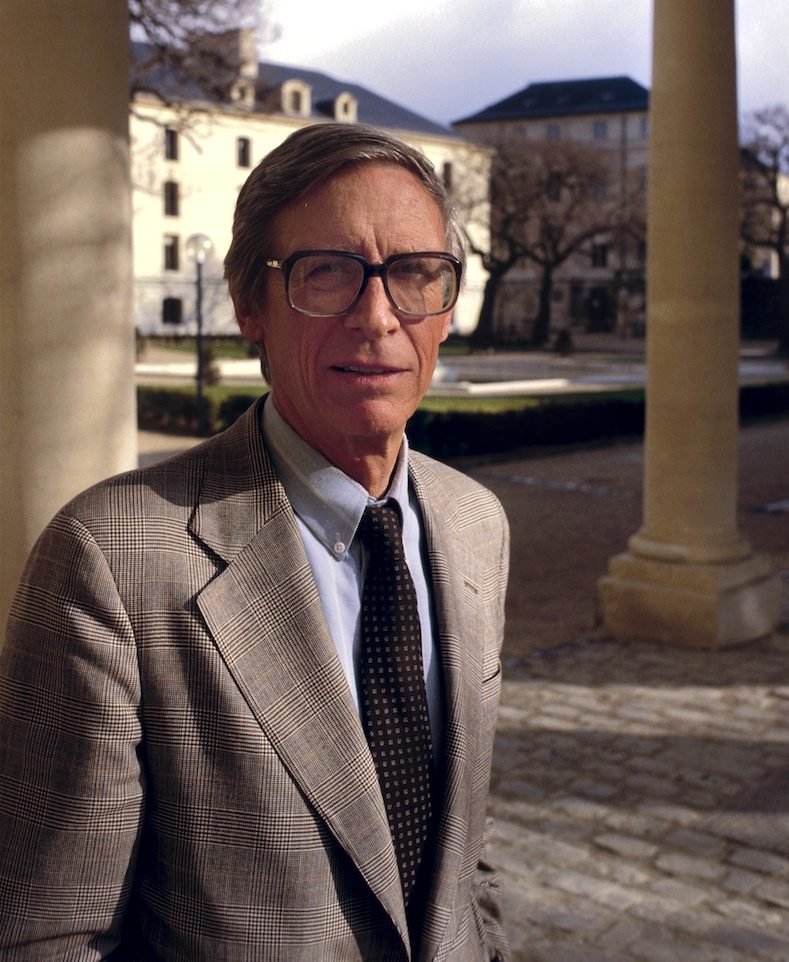 a man in glasses stands near pillars