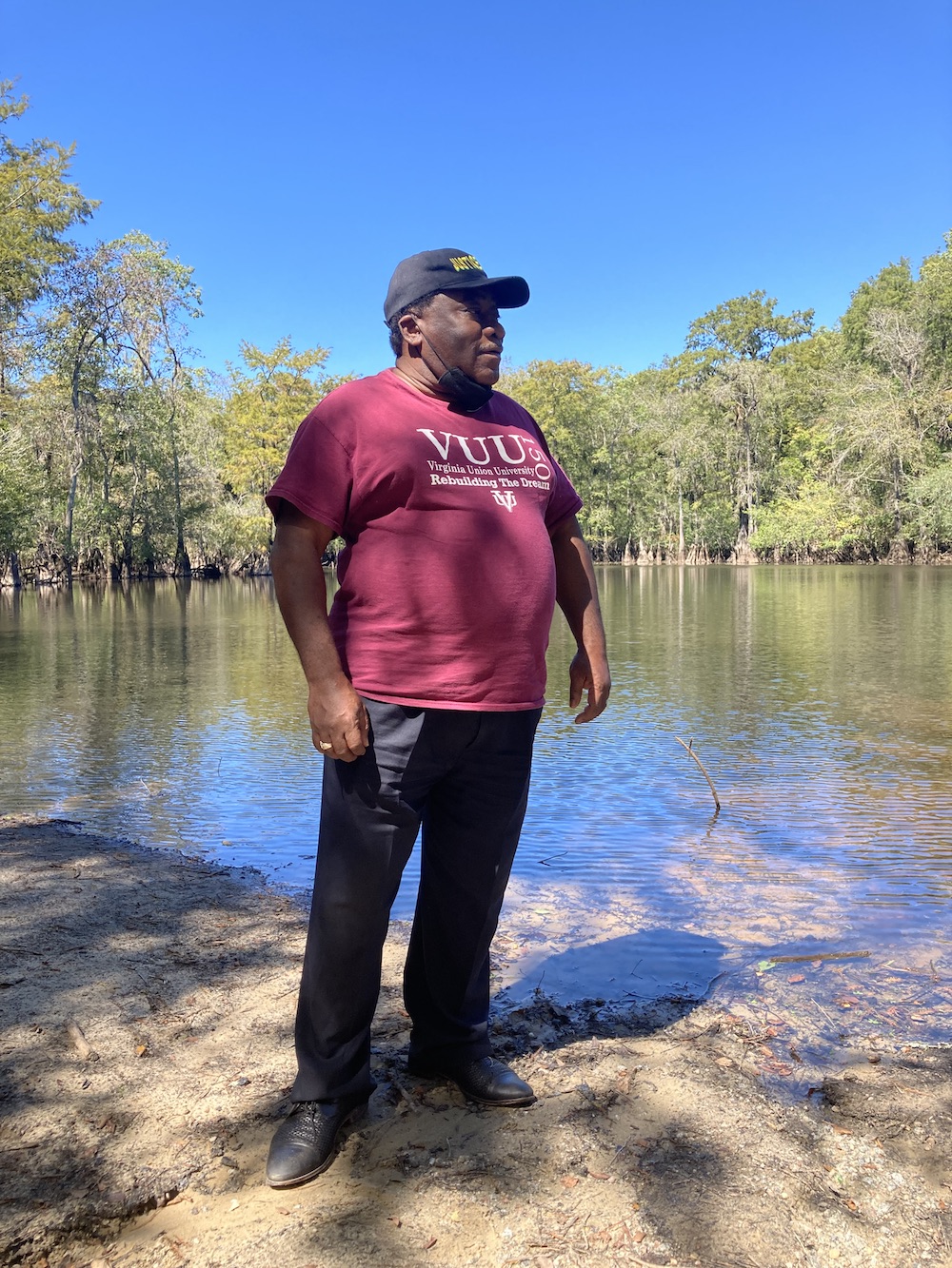 a man in a red shirt and hat stands in front of green trees