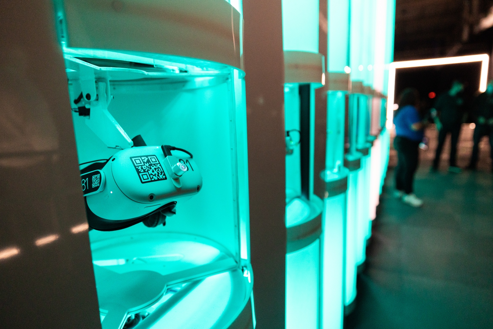 White headsets lit by teal lights are lined up across a wall.