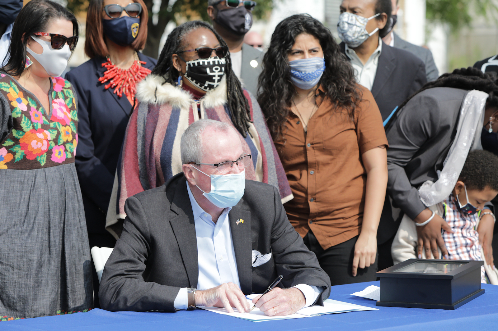 man signs paper while flanked by a crowd of people