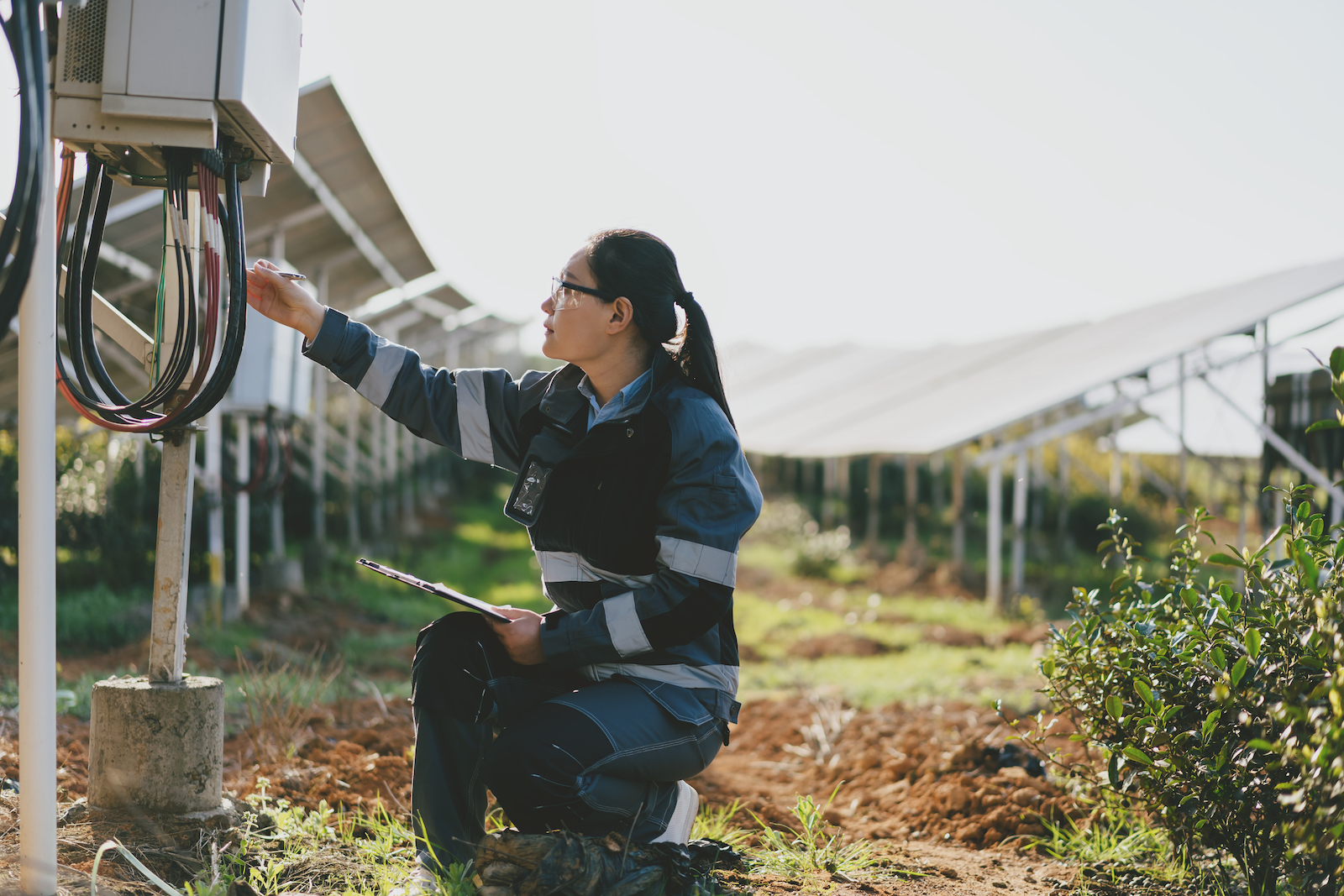 a woman kneels near solar panels wearing protective gear