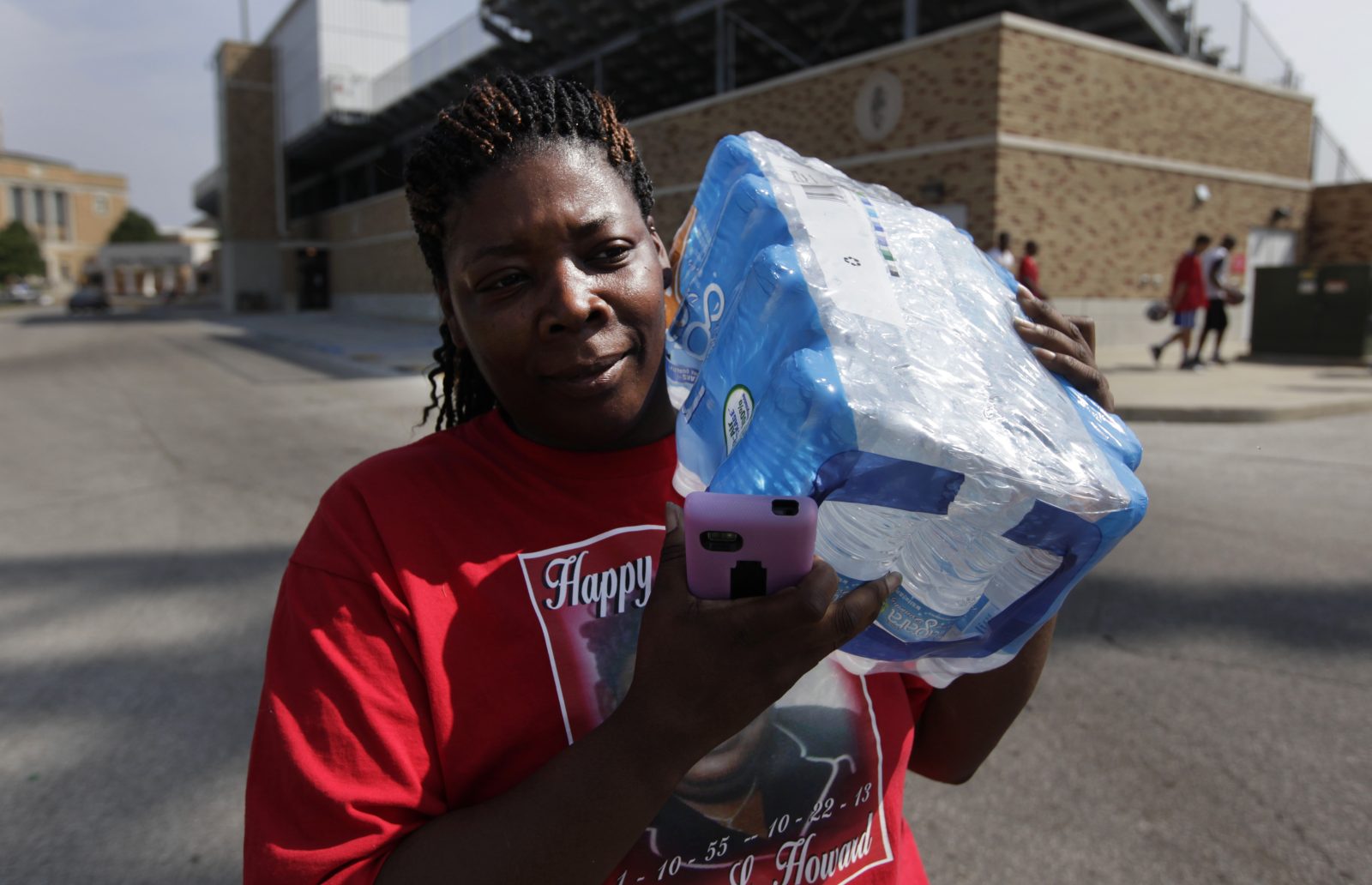 A woman carries a case of bottled water on her shoulder