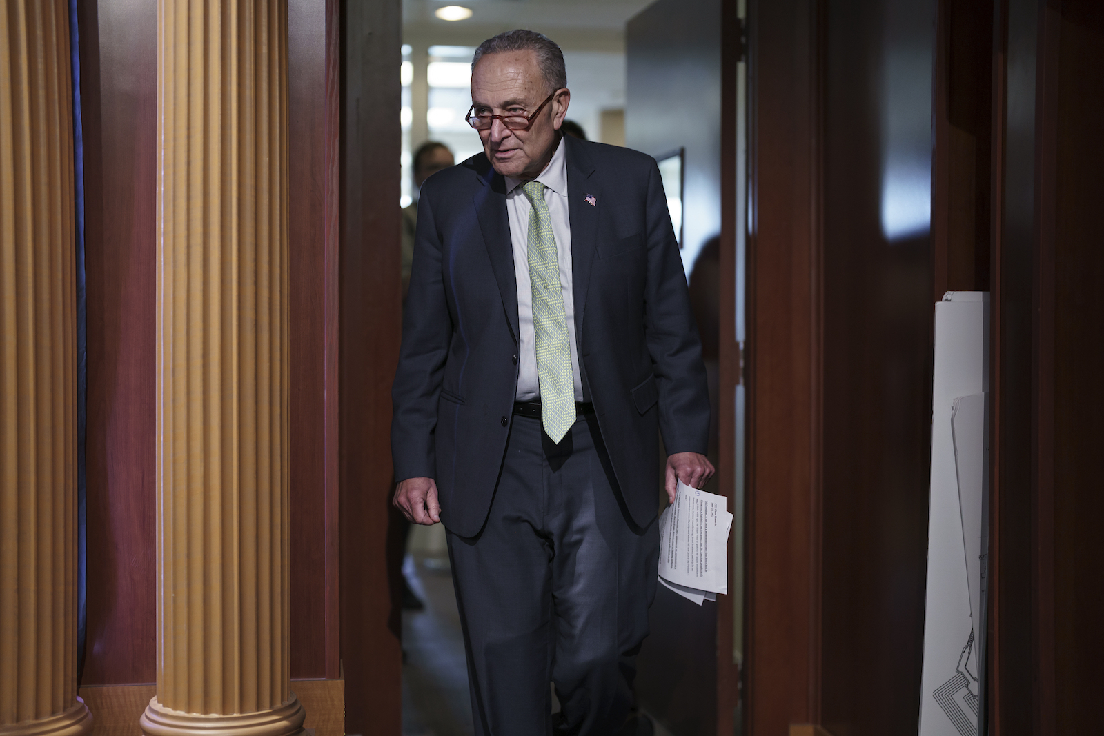 man wearing suit, tie, and glasses walks through doorway