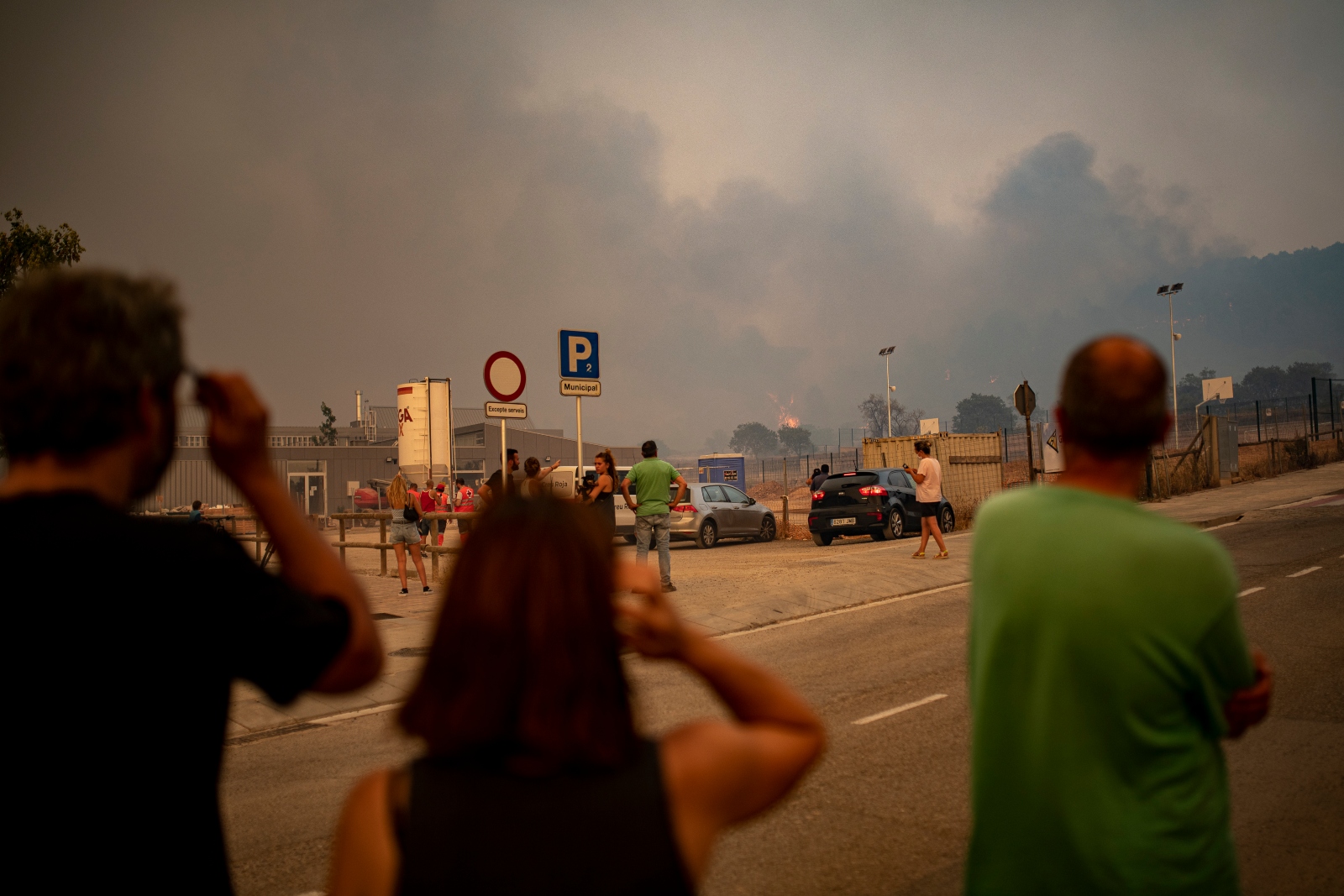 Three individuals in the foreground look out towards the horizon, which is filled with smoke. Sunlight filtering through the smoke gives the entire photo an orange tinge.