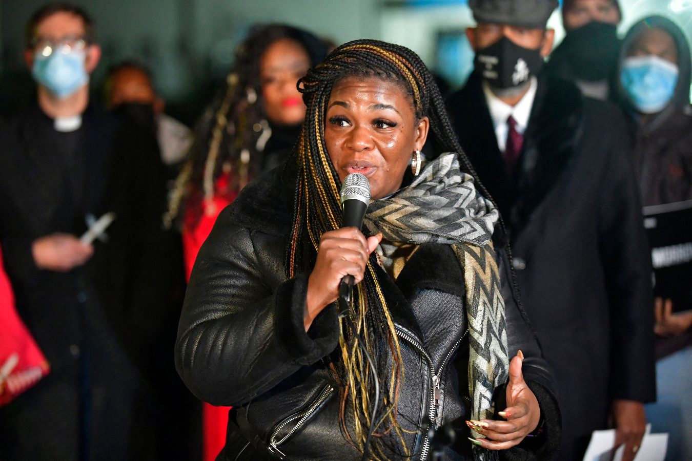 A congresswoman with long hair speaks via a microphone in front of a small crowd.