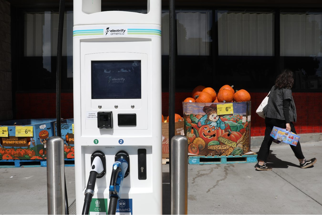 A woman with a bag walks past an electric car charging station in front of a building