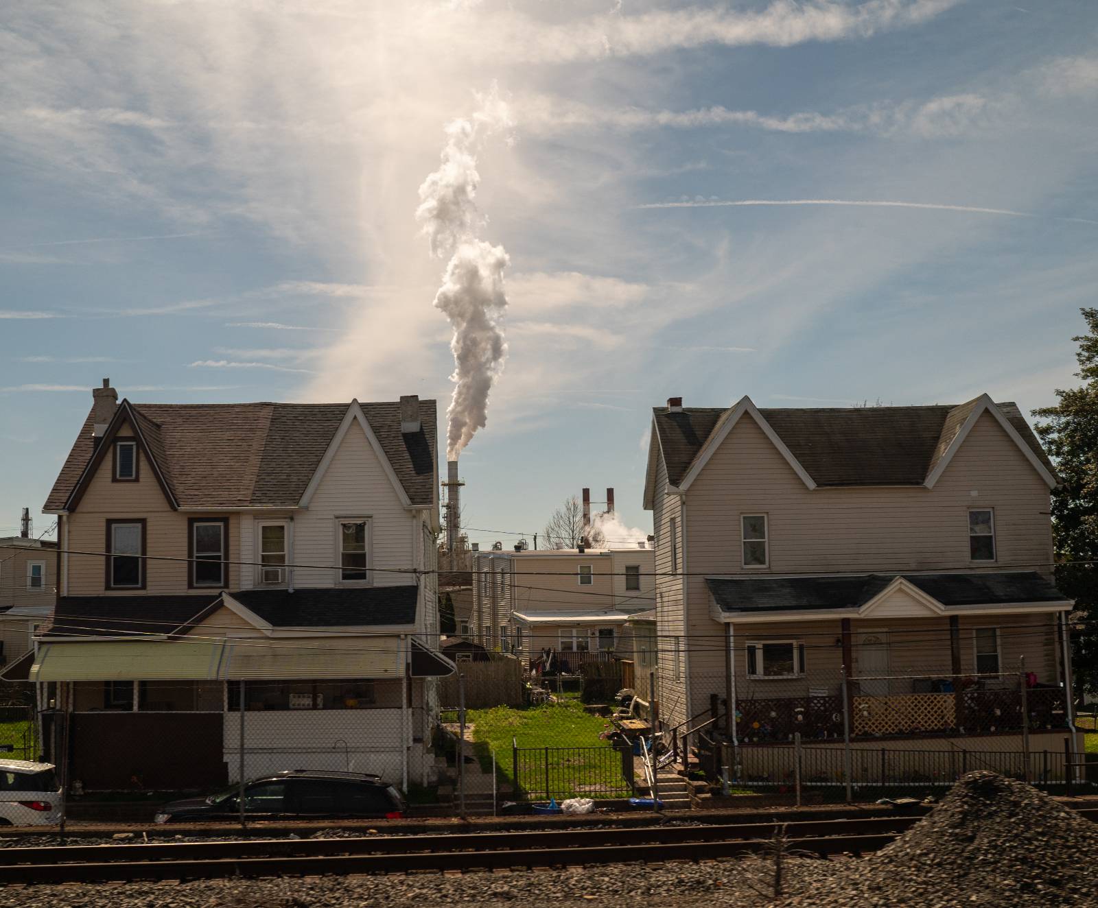 two houses on a street with a plume of white smoke from an industrial stack behind them