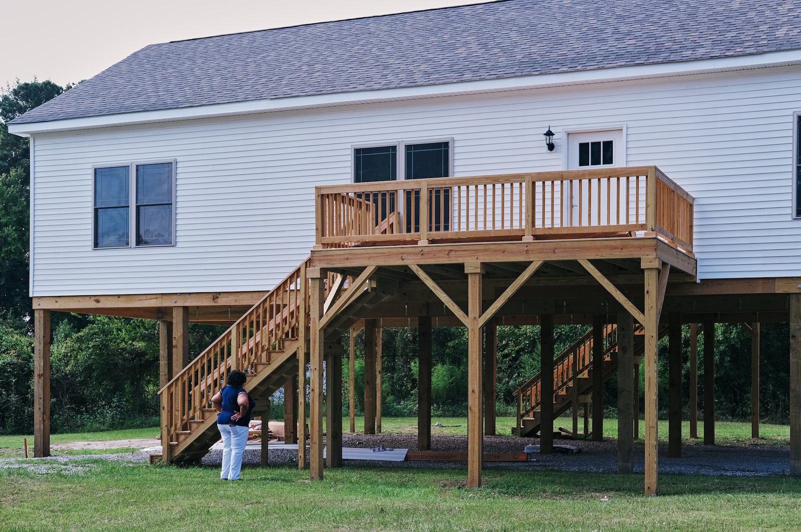 a woman looks up at a raised house connected to the ground by stairs