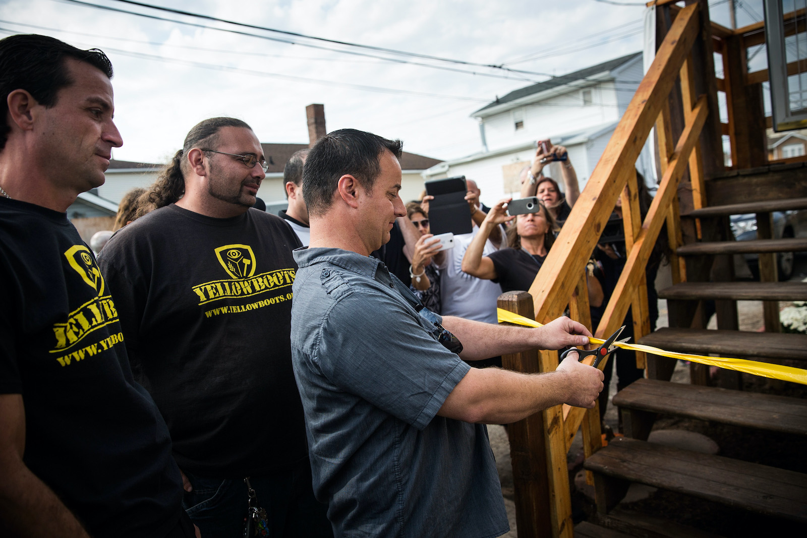 a man cuts a ribbon a stairway railing while surrounded by happy people