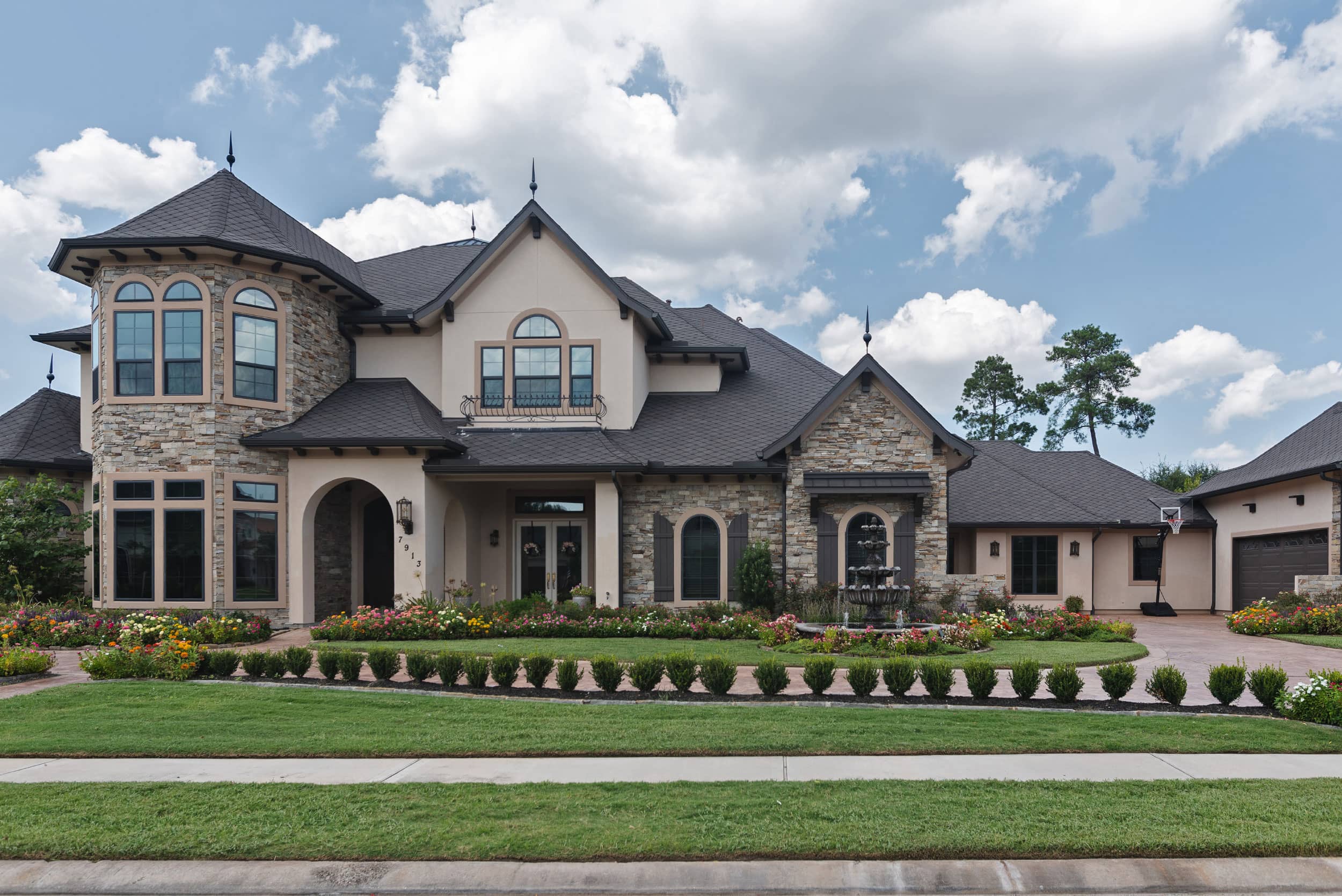 A large house with many rooms and windows with a very large landscaped lawn with flowers and decorative shrubs