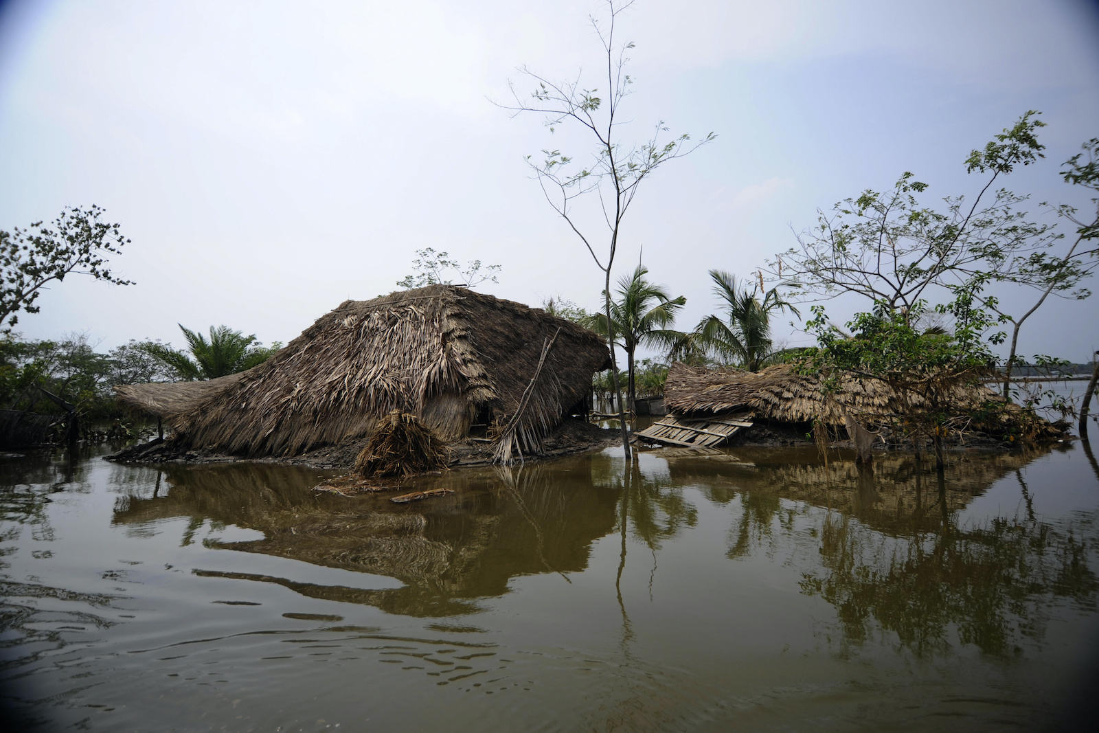 a damaged straw and wood house standing in a puddle