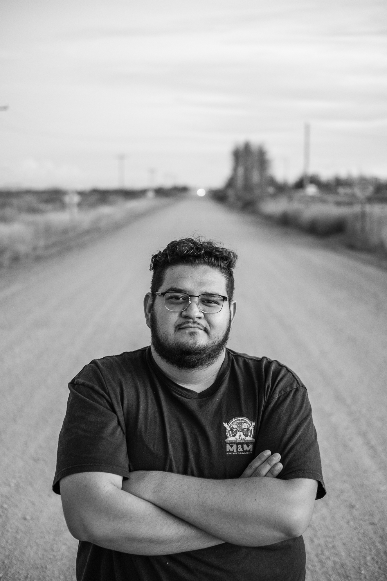 a man in a t-shirt stands in the middle of a dusty dirt road