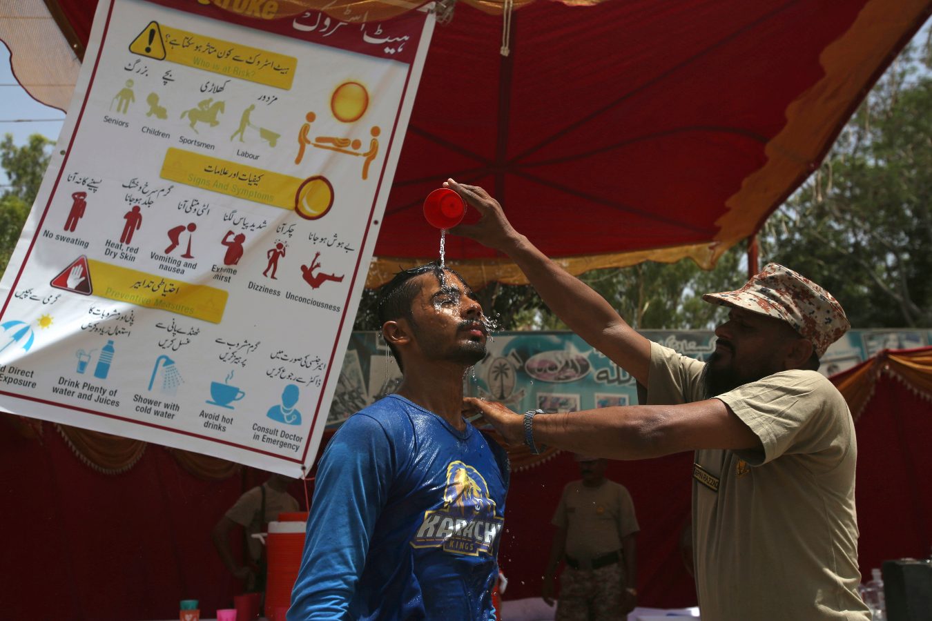 a man in a wet blue shirt gets water poured over his head by a man in a uniform