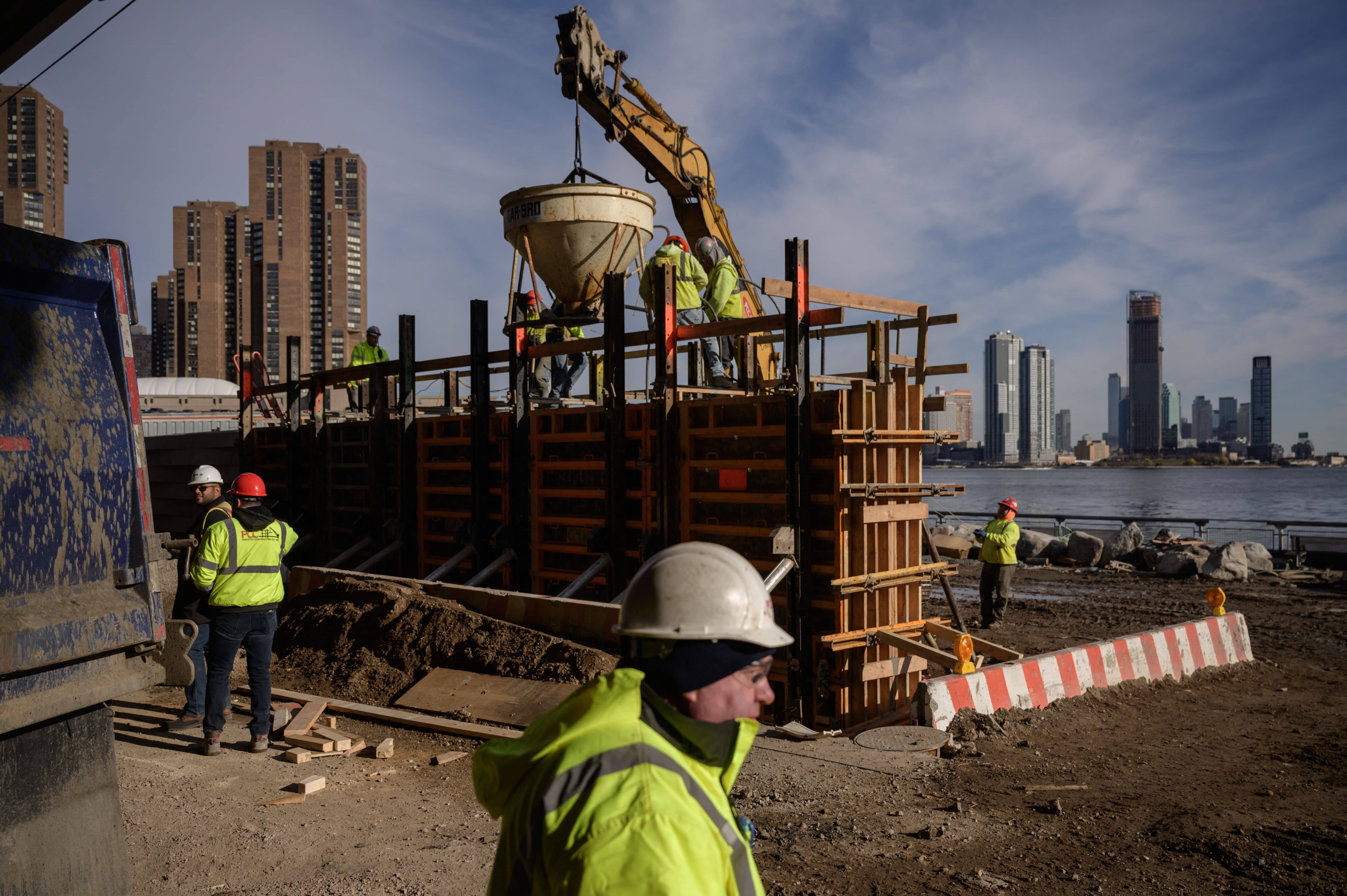 construction works walk around a site where a wall is in construction and in the background the city is visible across the water