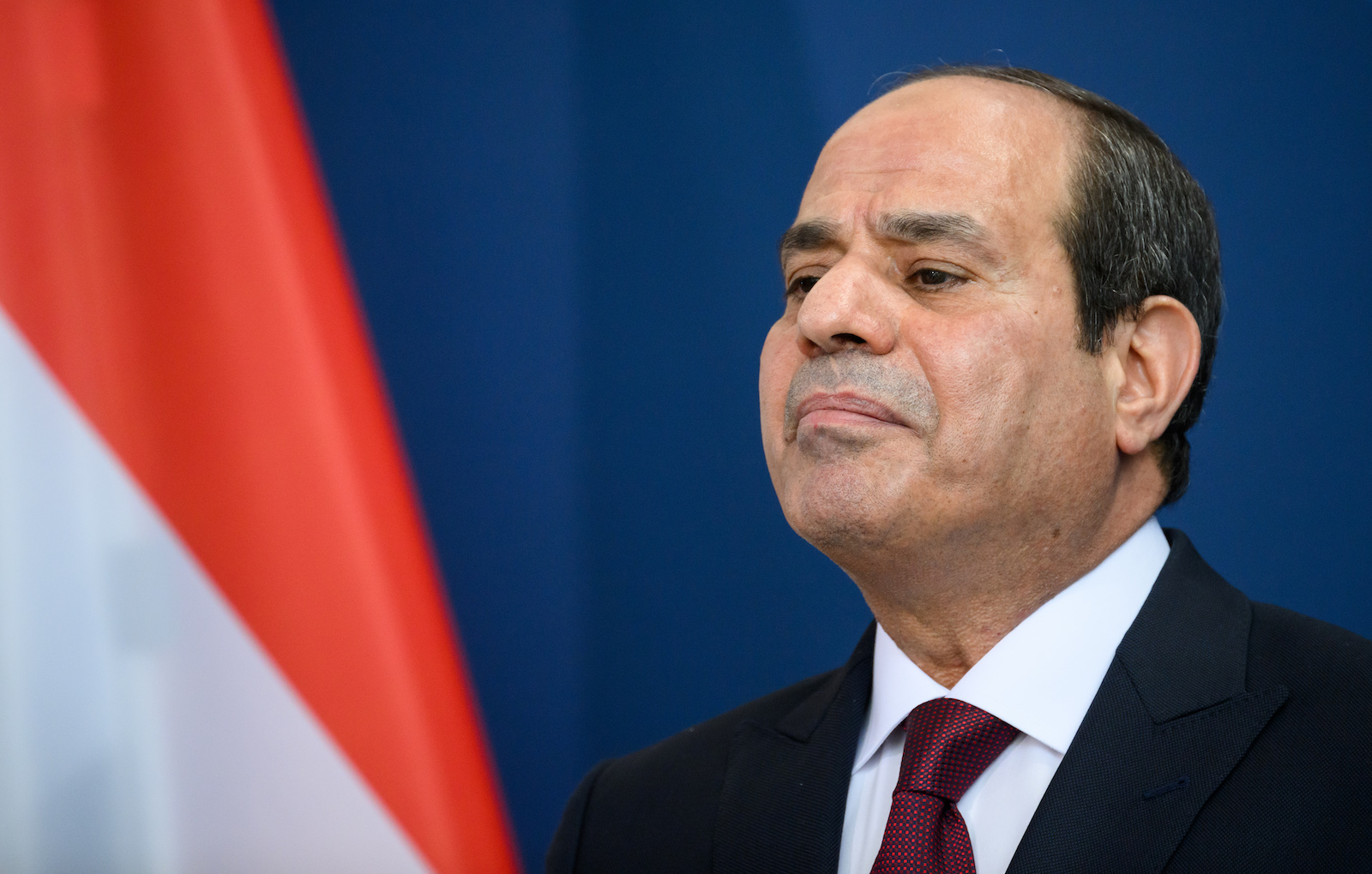 a man in a suit and tie stands near a flag