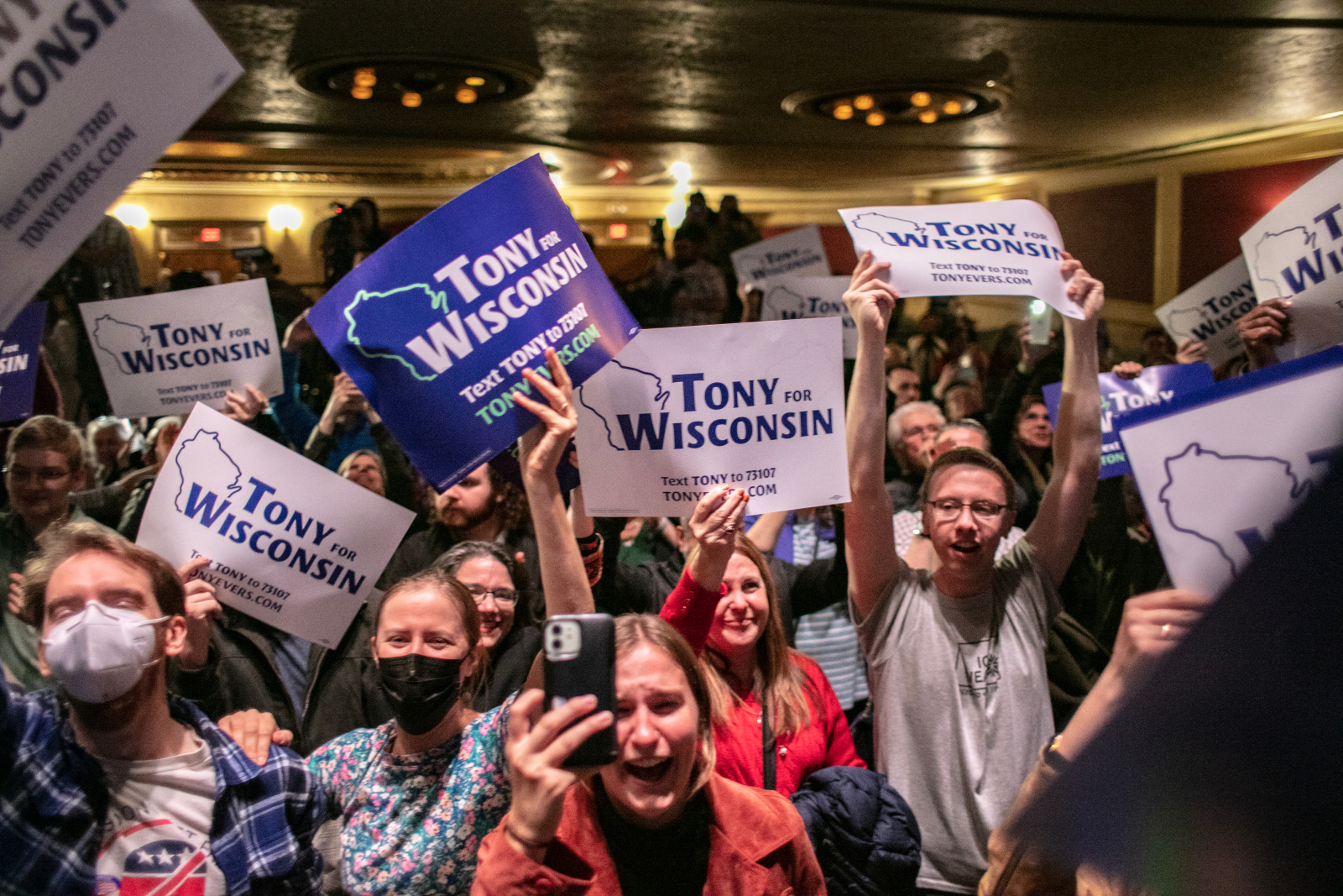 Varied people, mostly white, hold blue and white signs that read 