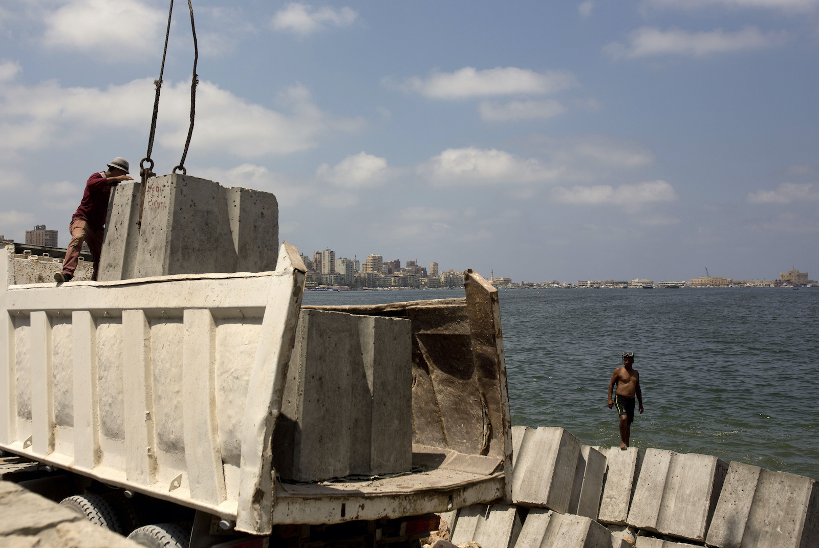 a construction crane moves big blocks of concrete onto a sea wall