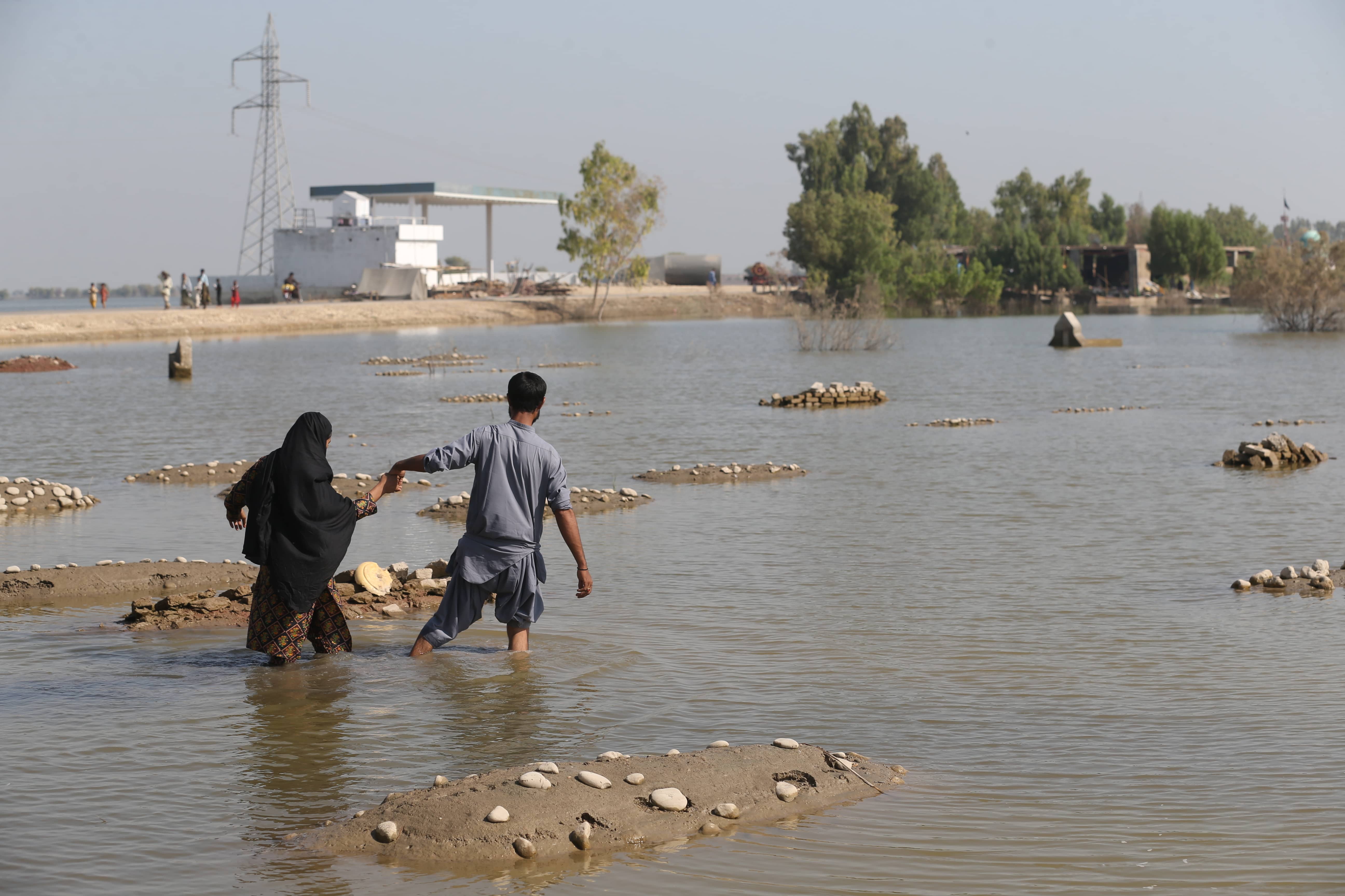 two people hold hands and cross a flooded landscape in the Sindh Province of Pakistan