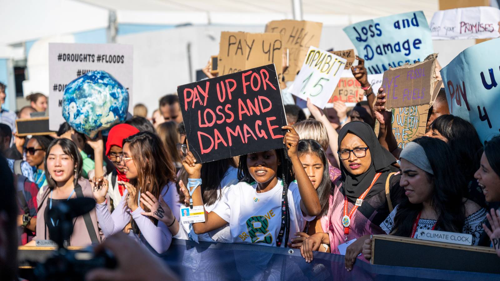 protestors hold up signs calling for wealthy countries to pay for loss and damage