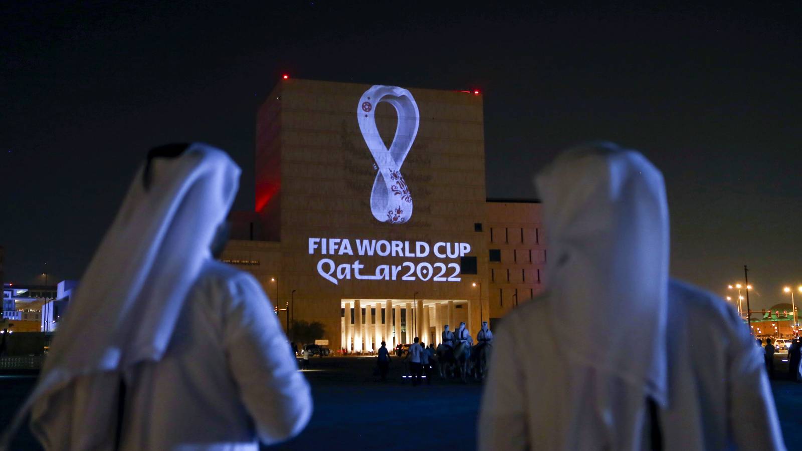 People gather to look at logo of 2022 FIFA World Cup projected onto building.