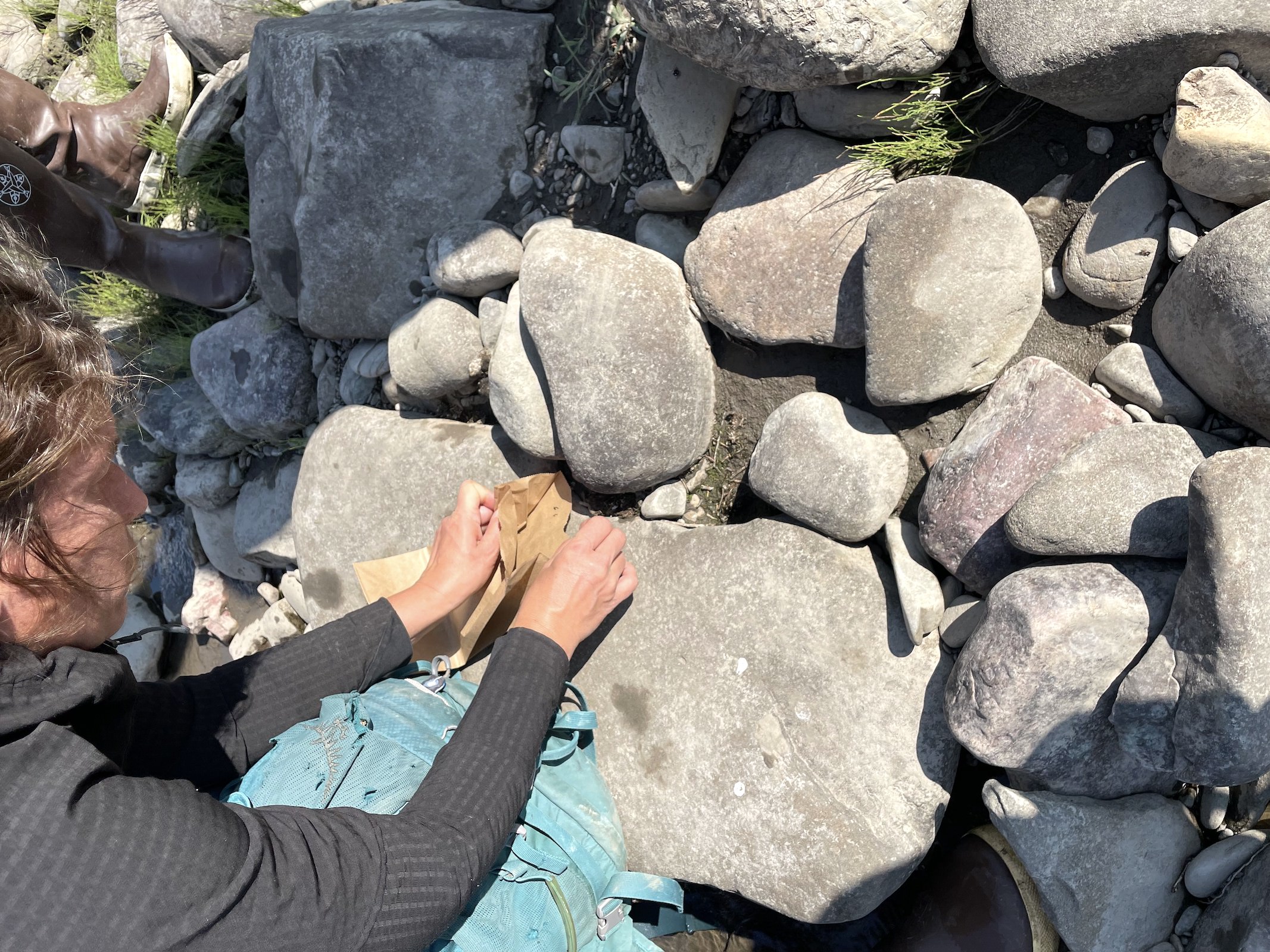 a person kneels near rocks holding a small brown paper bag