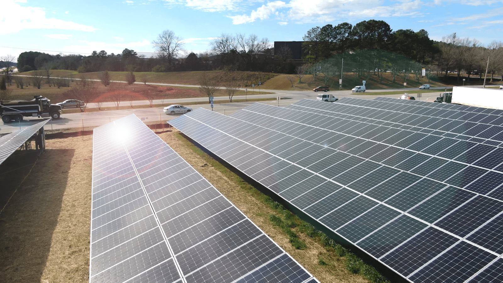 the sun shine off a row or large solar panels in a grassy area next to a road with cars