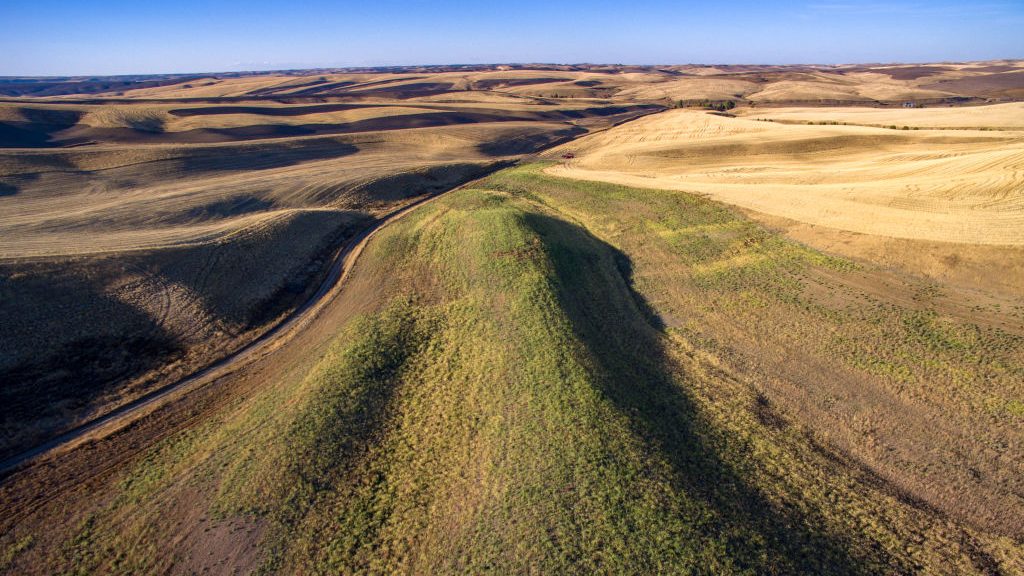 a photo of hills where the one in the foreground is covered in green