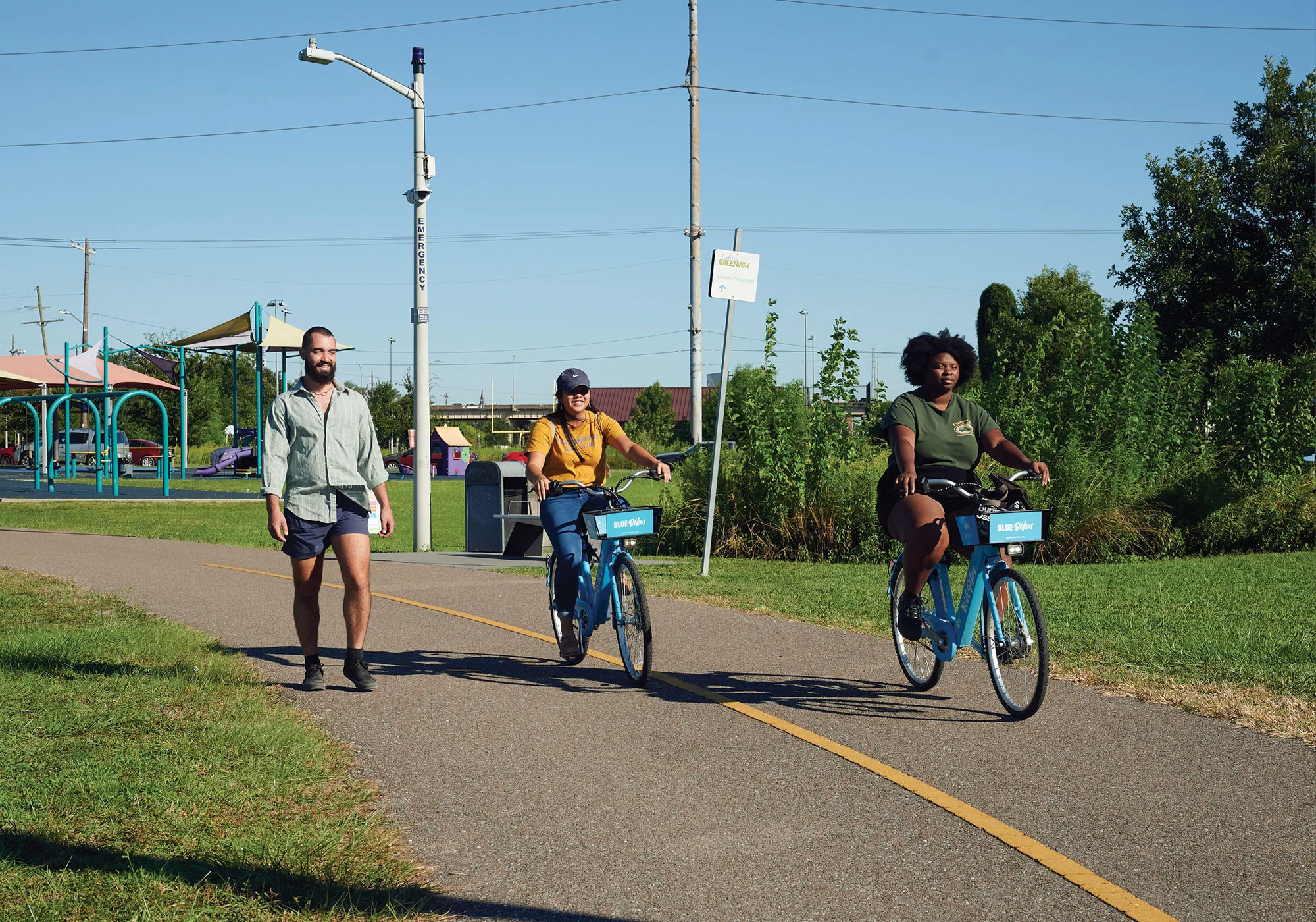 Two cyclists on Blue Bikes ride down a park path