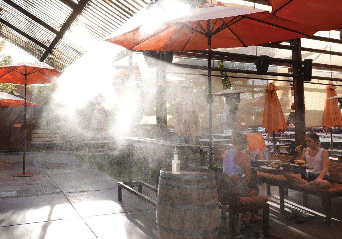 Two people eat outside below umbrellas and water misters