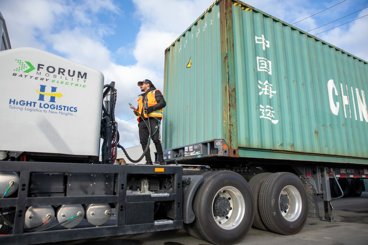 a man in an orange vest holds a coupler between two parts of a truck