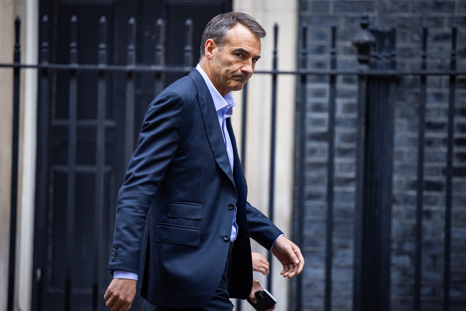 An executive in a suit walks in front of a wrought iron gate with a worried look.