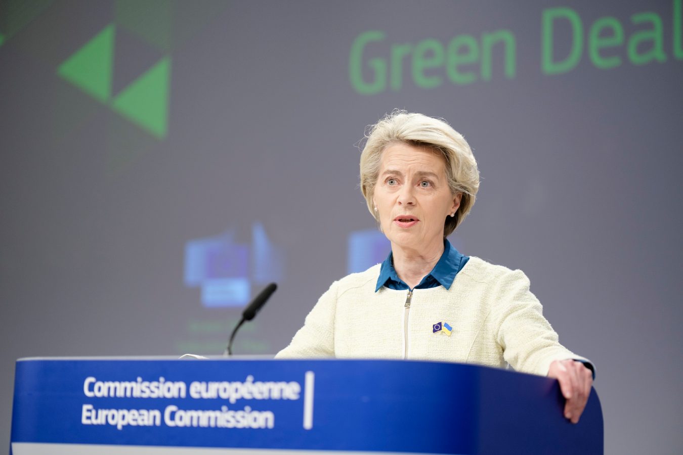 A woman in white zip-up top stands at a blue podium with the words 