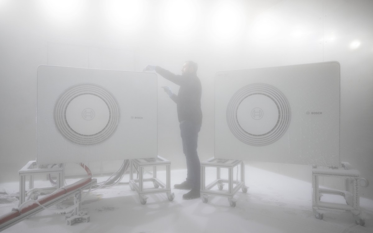 A worker examines a heat pump in an icy chamber.