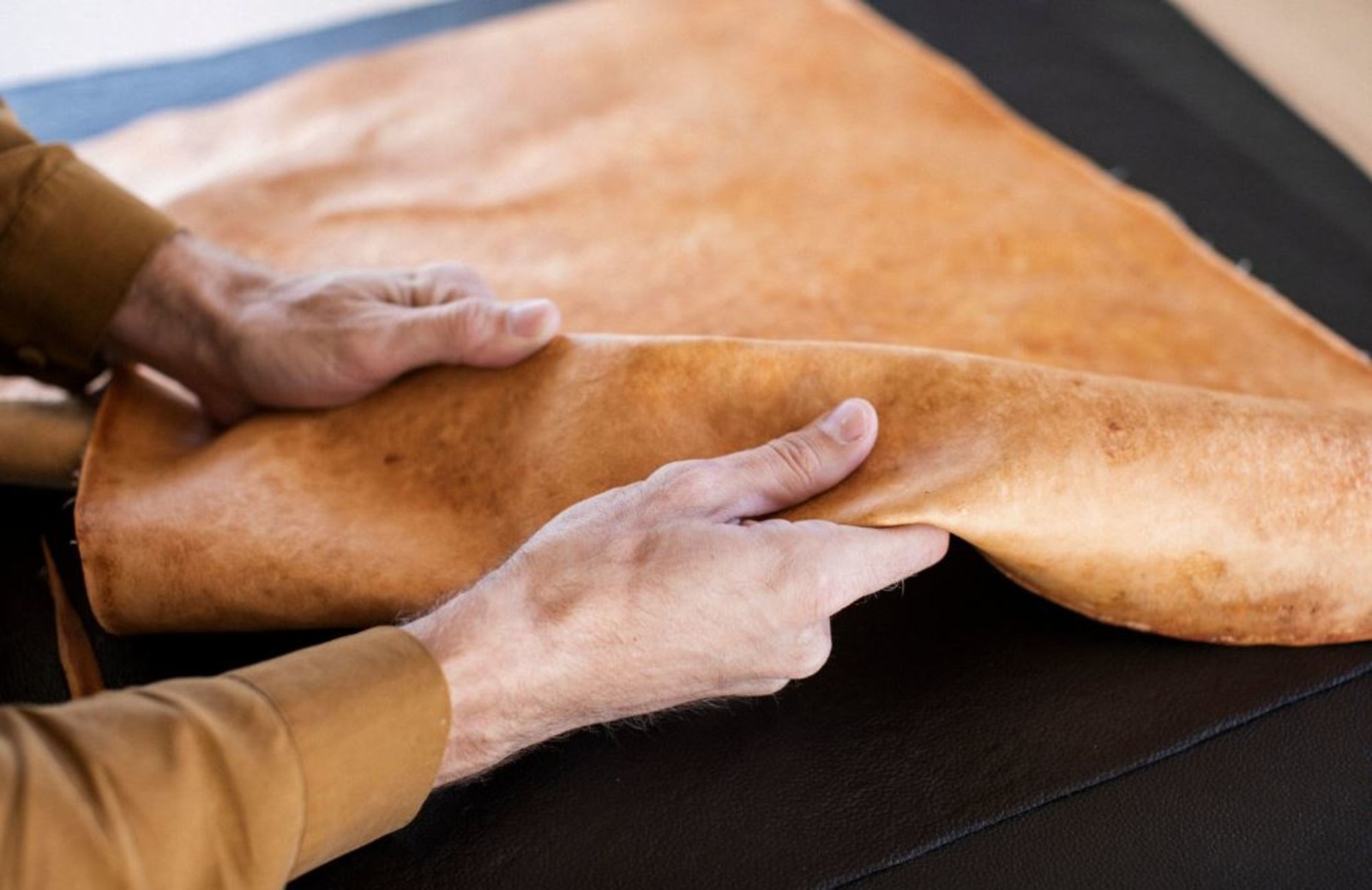 A person holds a piece of light brown leather that's made from mushrooms.