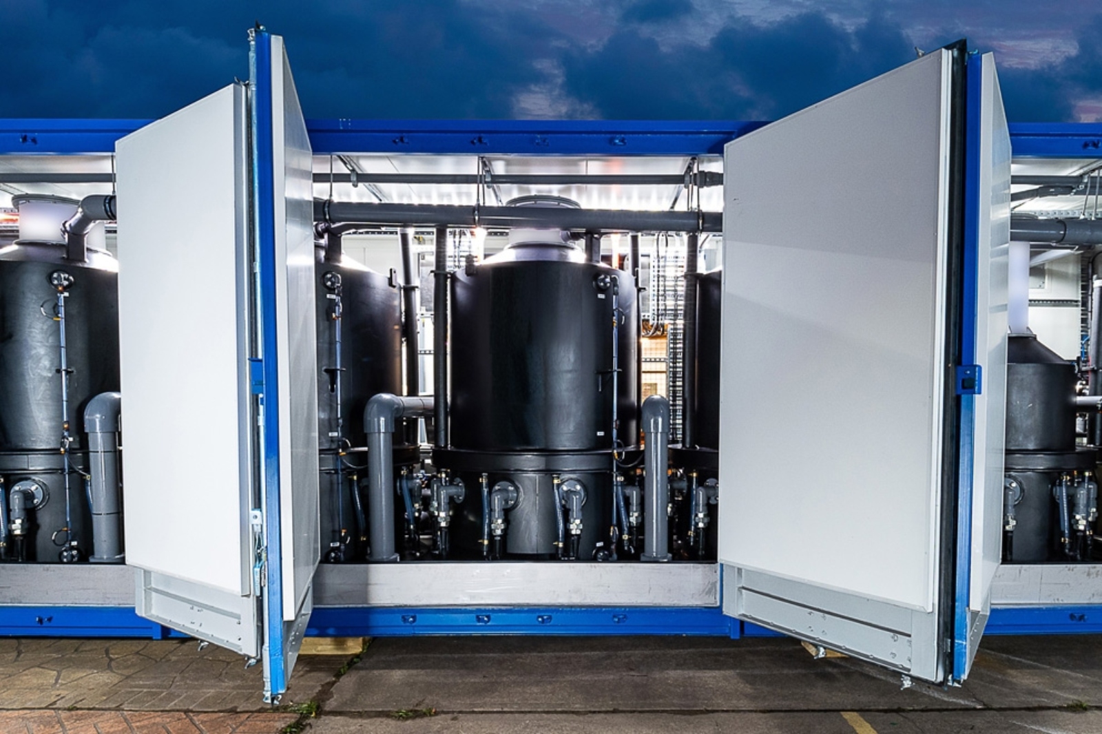 A set of gray pipes and a large metal water filter inside a white and blue container.