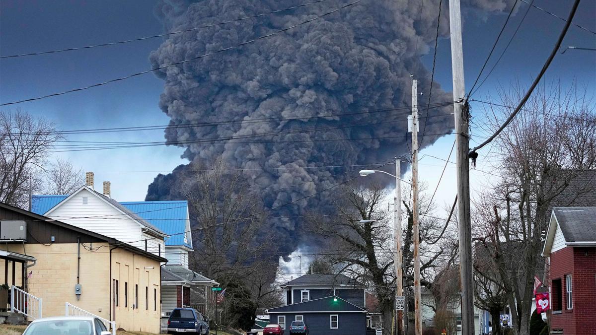 Enormous plume of black smoke billowing up into the sky behind houses on a residential street