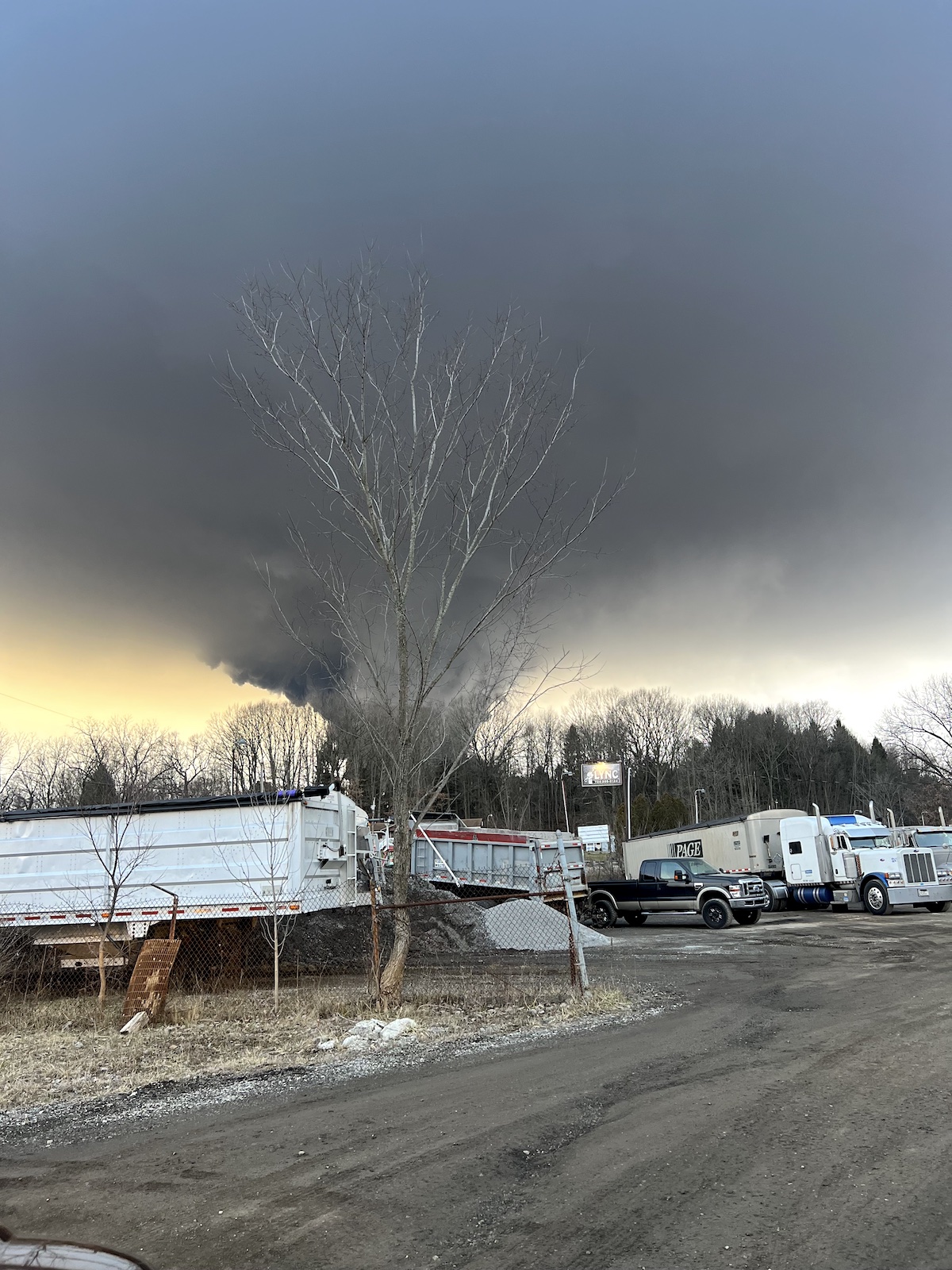 a large plume of black smoke fans out like a reverse tornado over a line of trcks