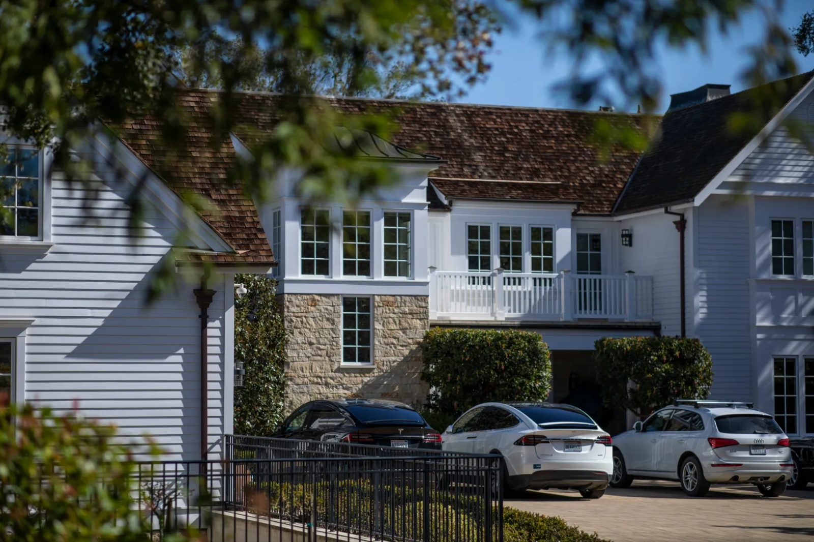 Th exterior of a mansion with three electric cards parked out front.