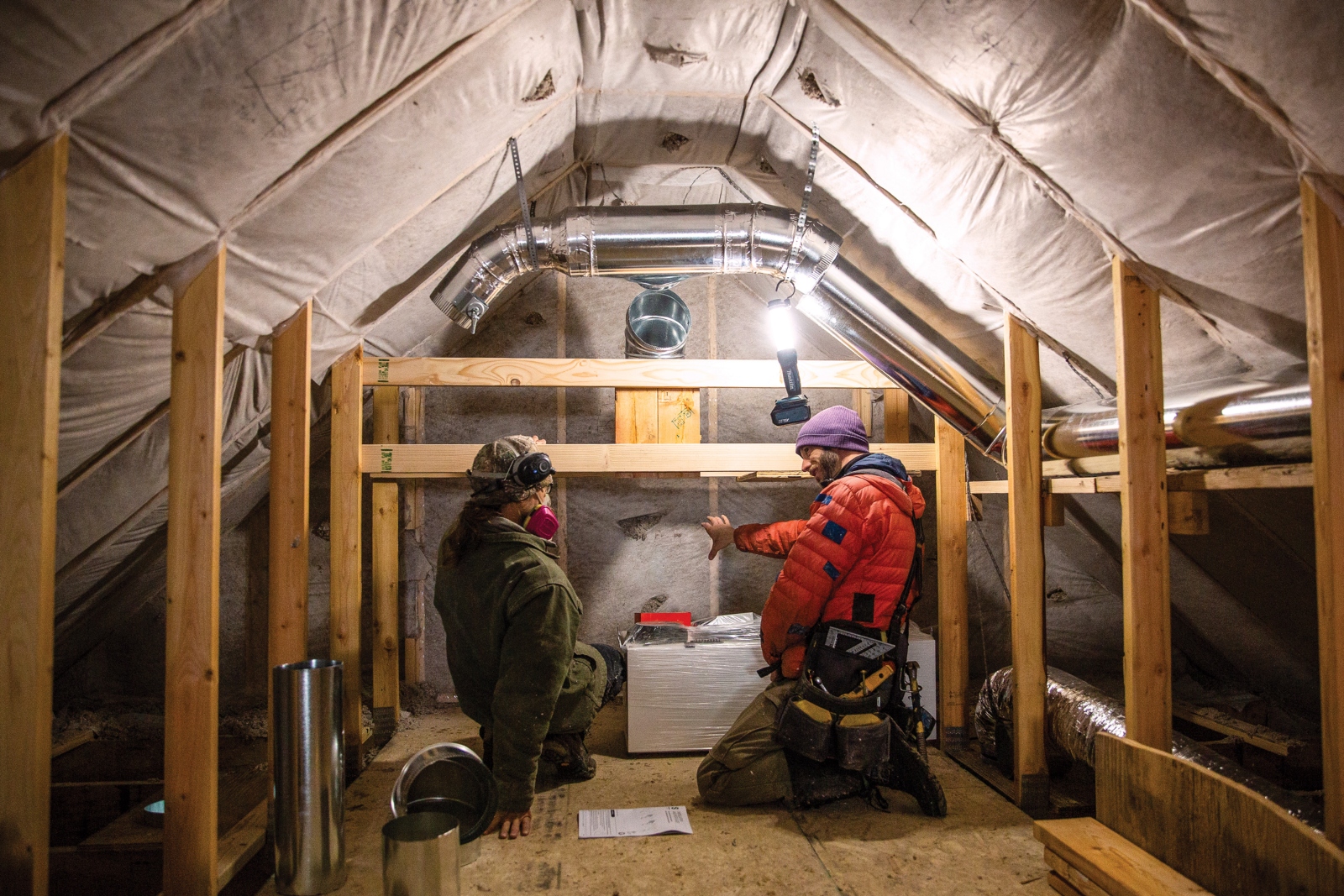 Two men kneel in an attic, while one wears a mask.