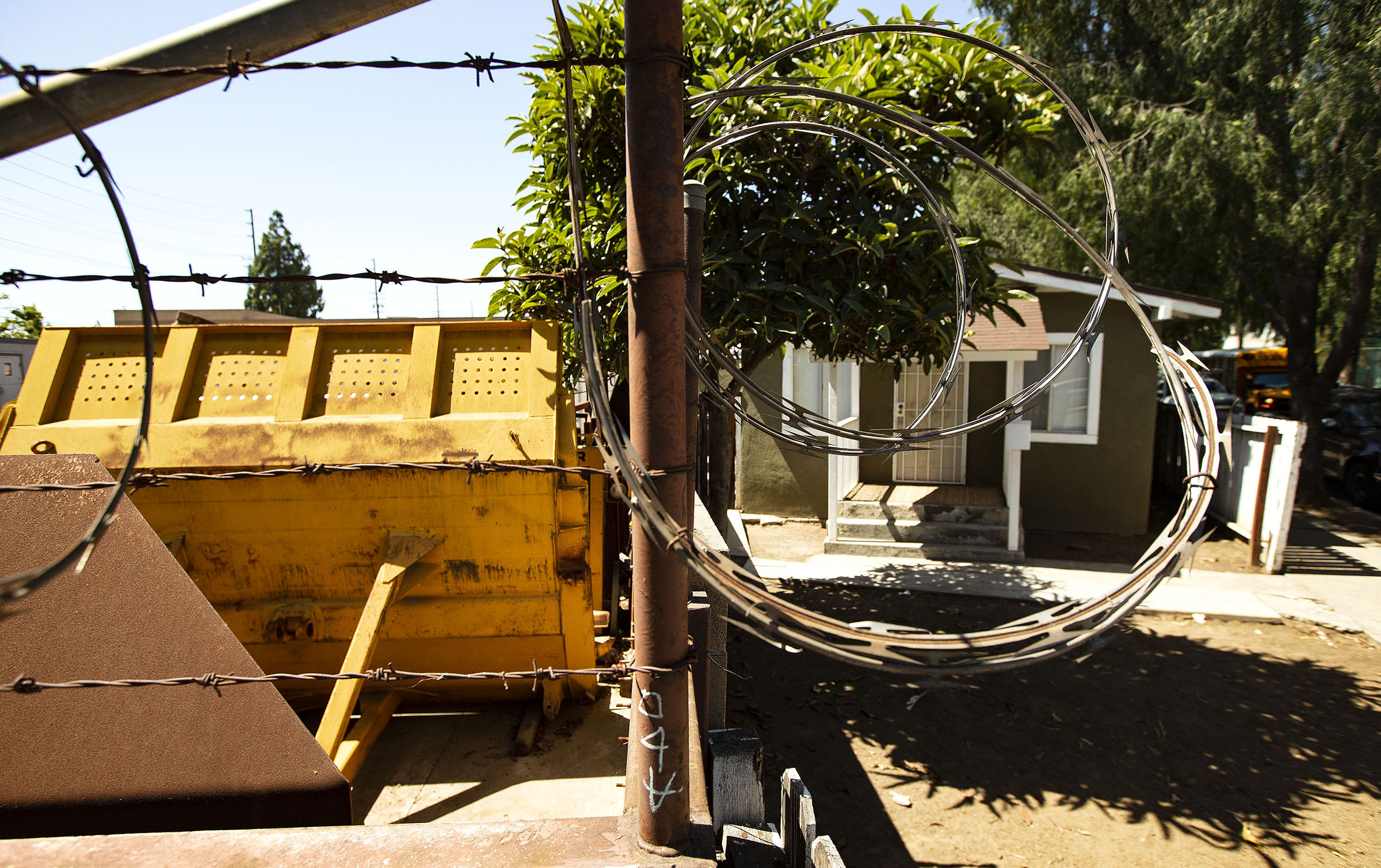 A barbed-wire barrier separates an industrial business and a residential home