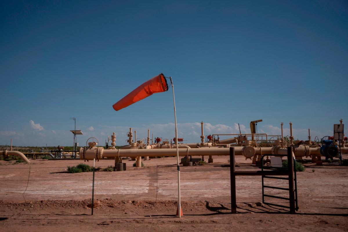 On a patch of brown sand, yellow pipes stretch into the distance with a red flag blowing in the wind in the foreground.