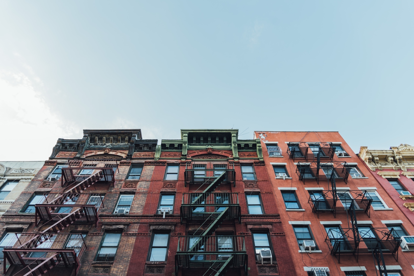 Three red-colored apartment buildings with fire escapes, as seen from below