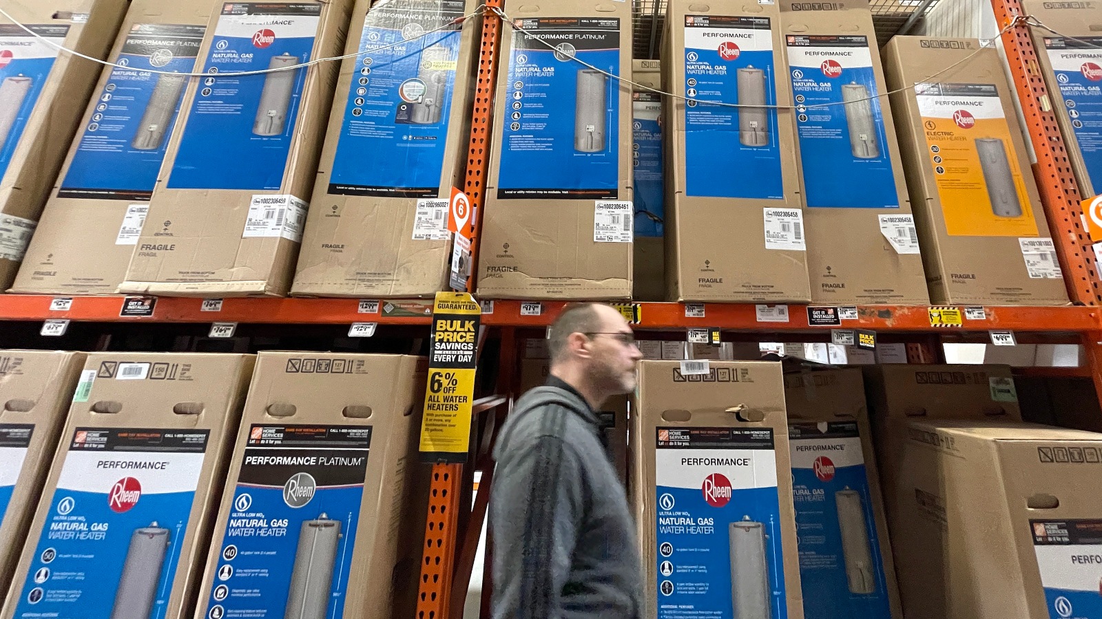 A man walks by shelves filled with heat pumps in an appliance store.