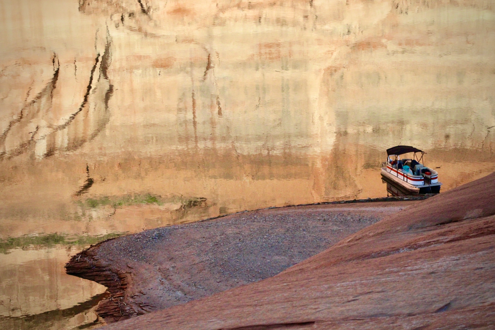 A small boat rests on a shallow lake with the cream-colored rocks reflected in the water.