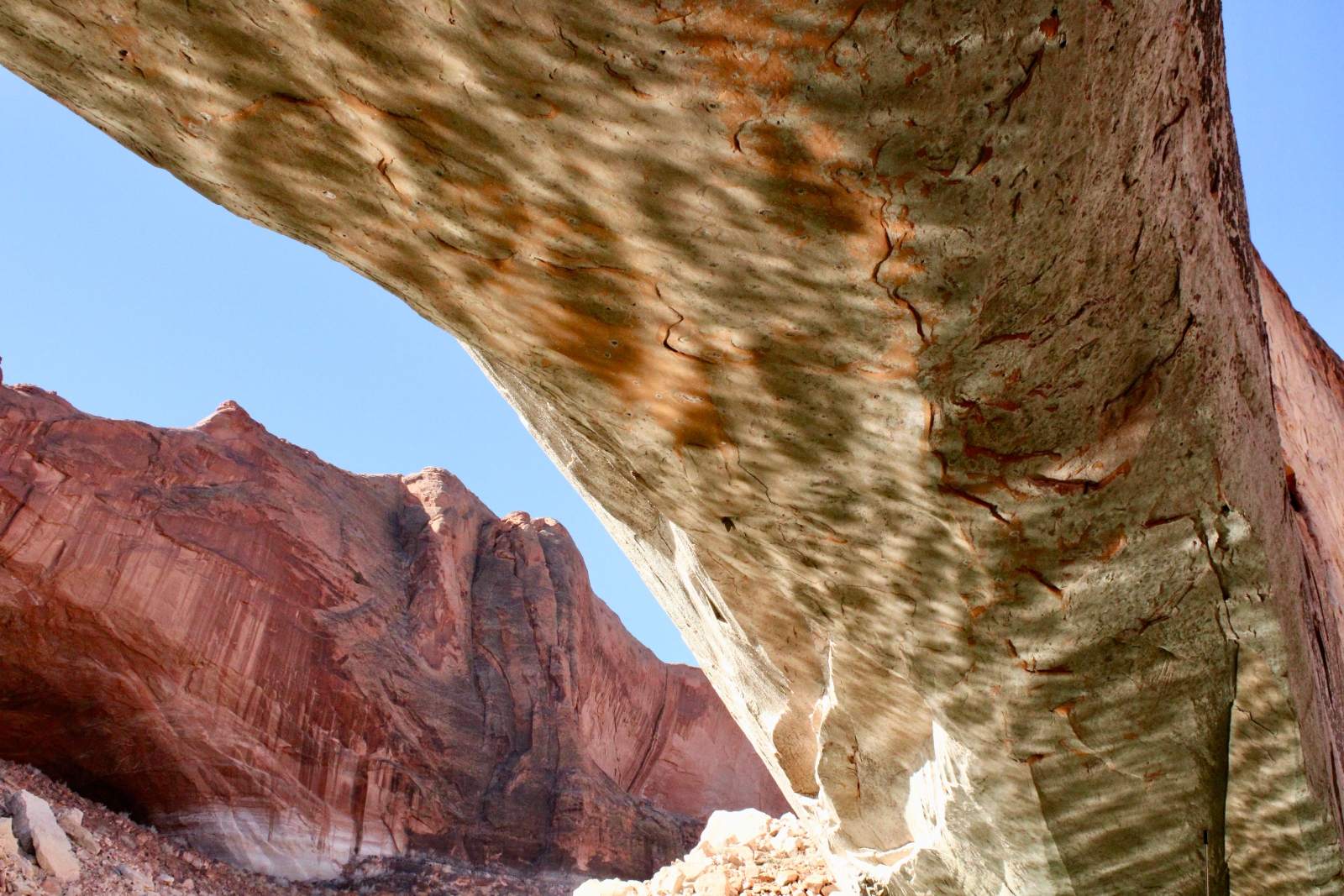 A bridge-like mass of red and tan rock rises next to a red mountain.