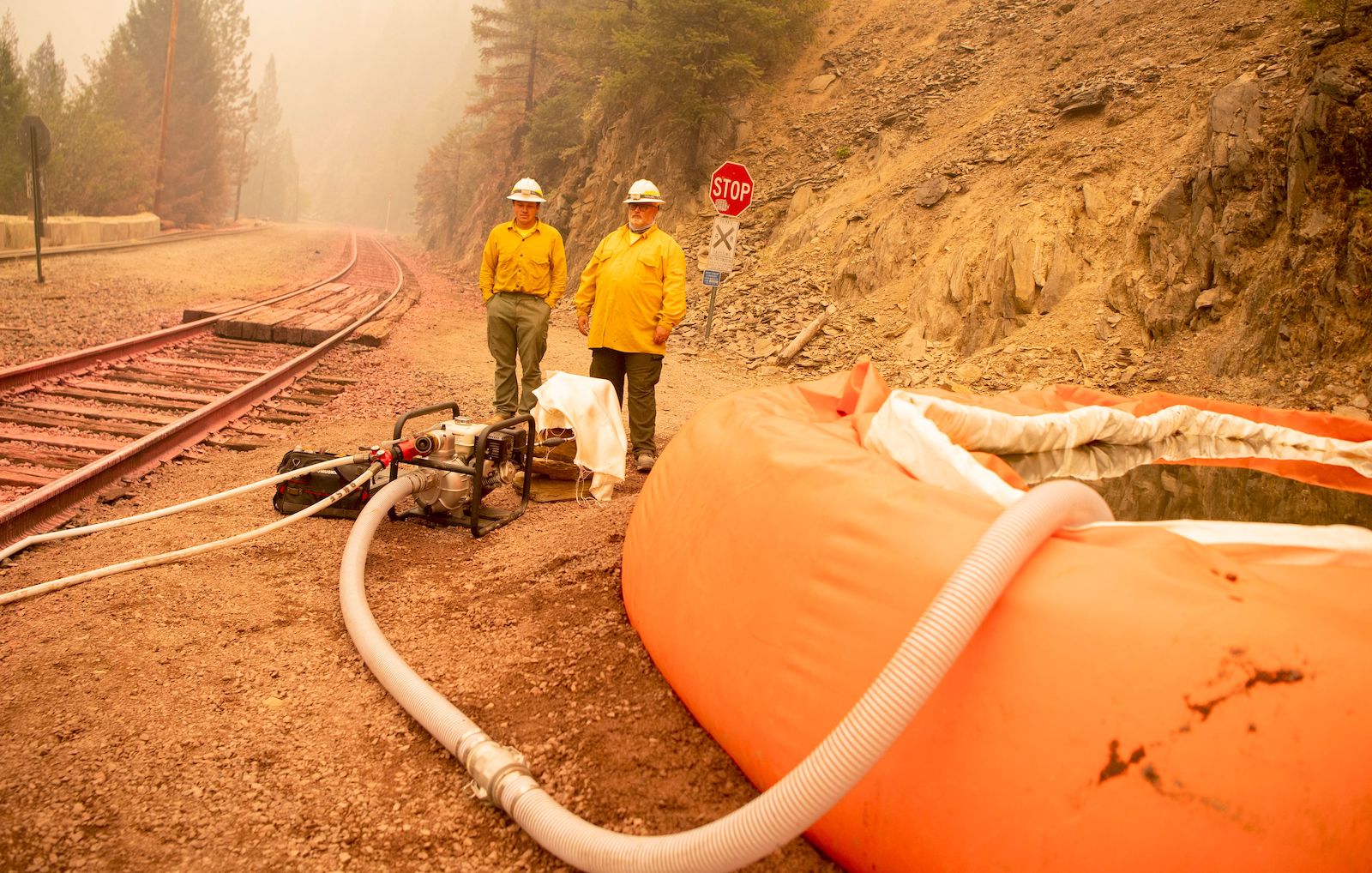 two men stand with a hose near train tracks