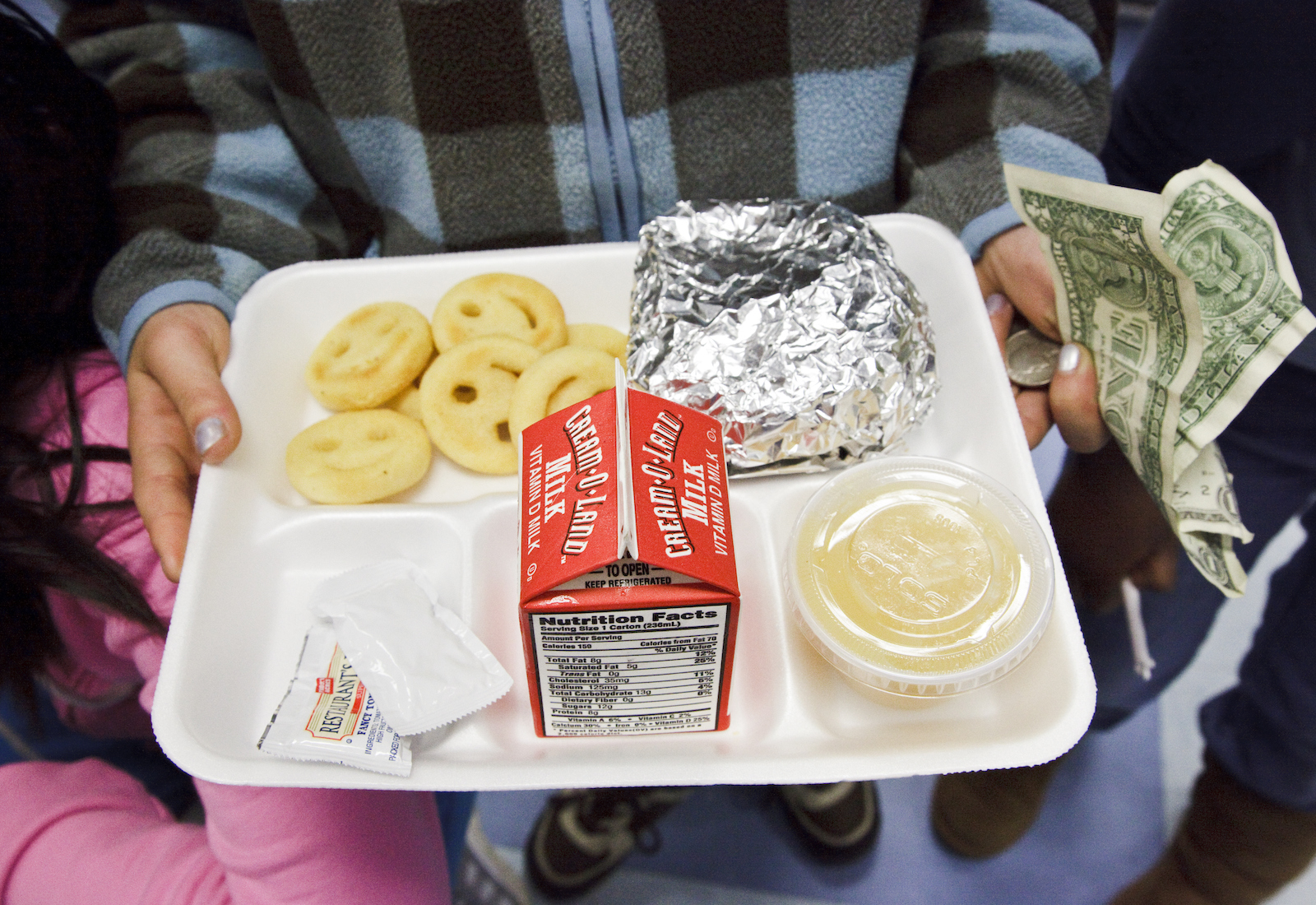 White tray with milk, smiley-faced french fries, apple sauce, and sausage